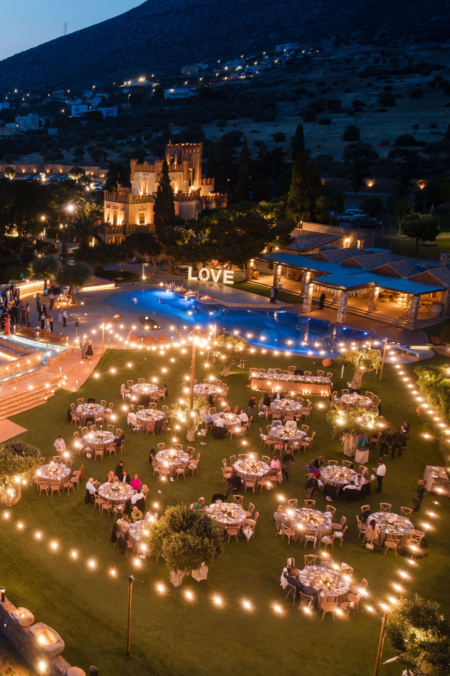 A stunning aerial view of an outdoor wedding reception with string lights and round tables under the stars.
