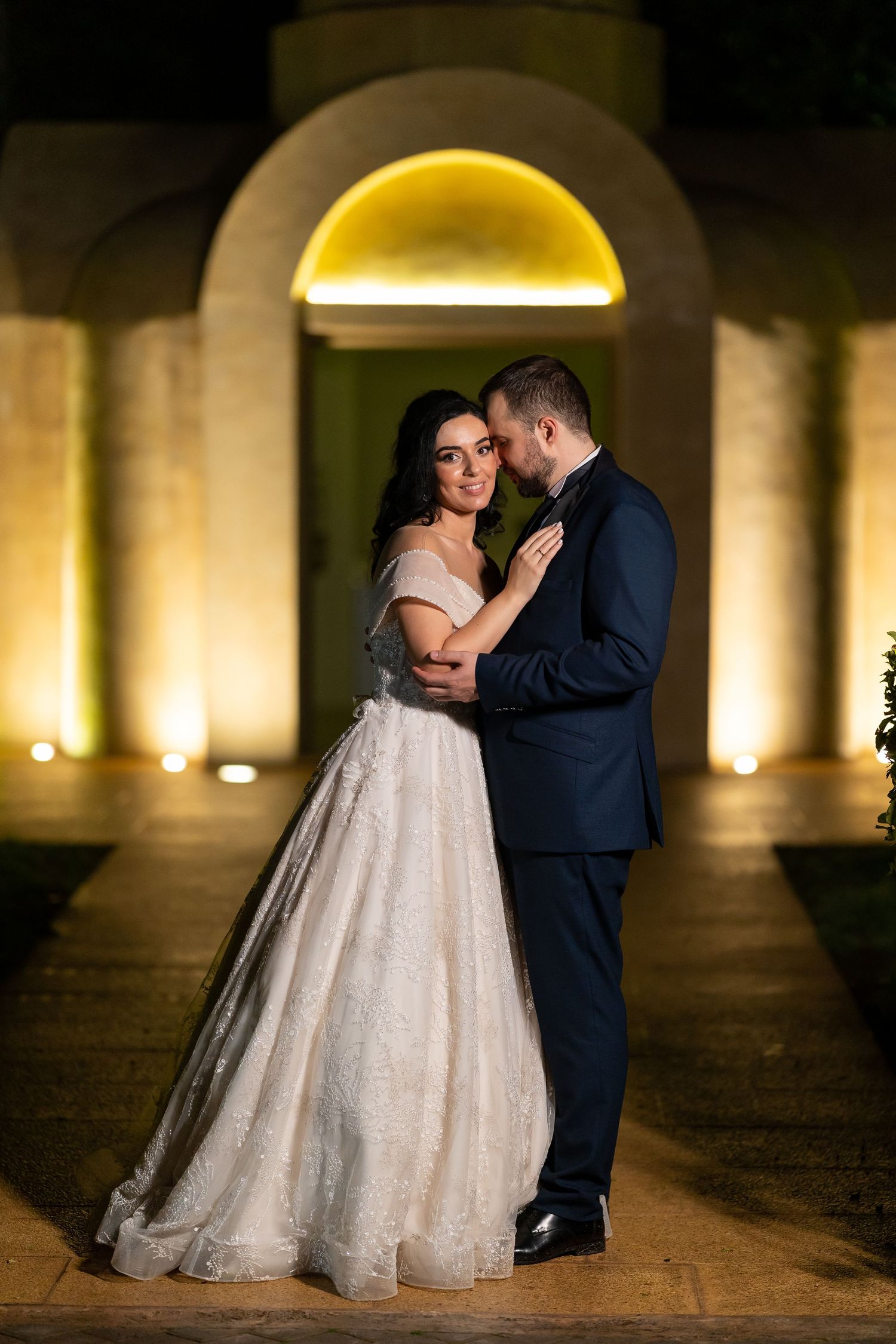 Romantic nighttime wedding photos under illuminated stone archways capturing intimate moments between newlyweds.