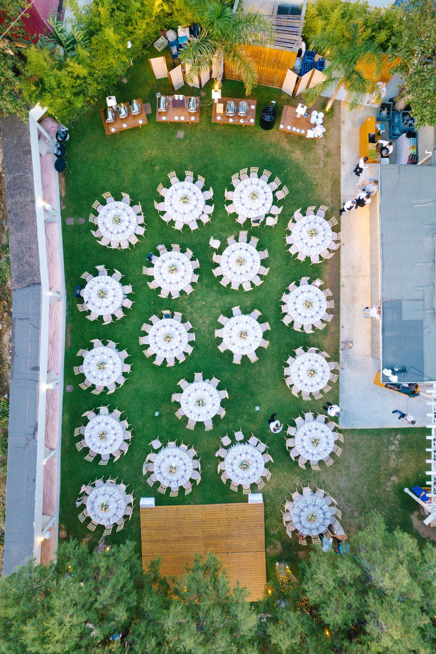 Aerial view of outdoor wedding reception with white round tables arranged on a green lawn.