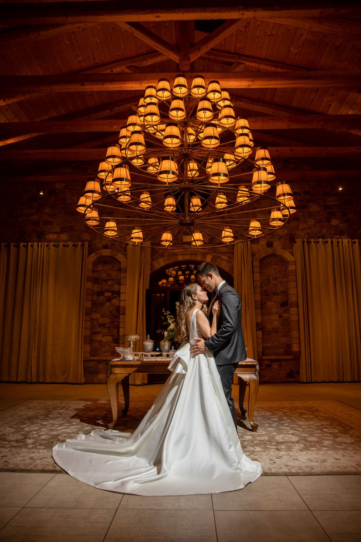 Romantic first dance in rustic venue with warm amber lighting and exposed wooden beams.