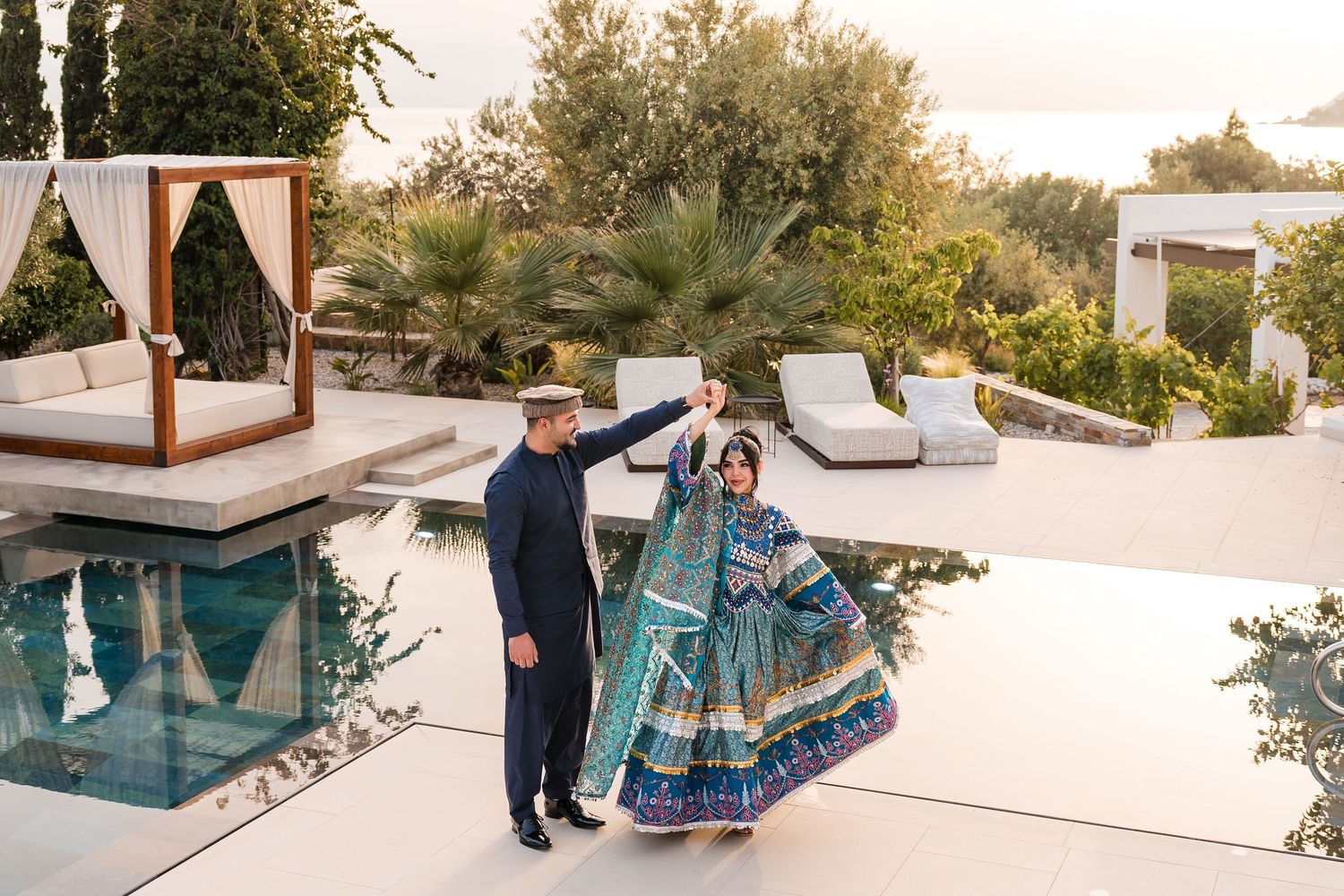 Couple in traditional Indian attire dancing by a luxury pool at an outdoor wedding venue.