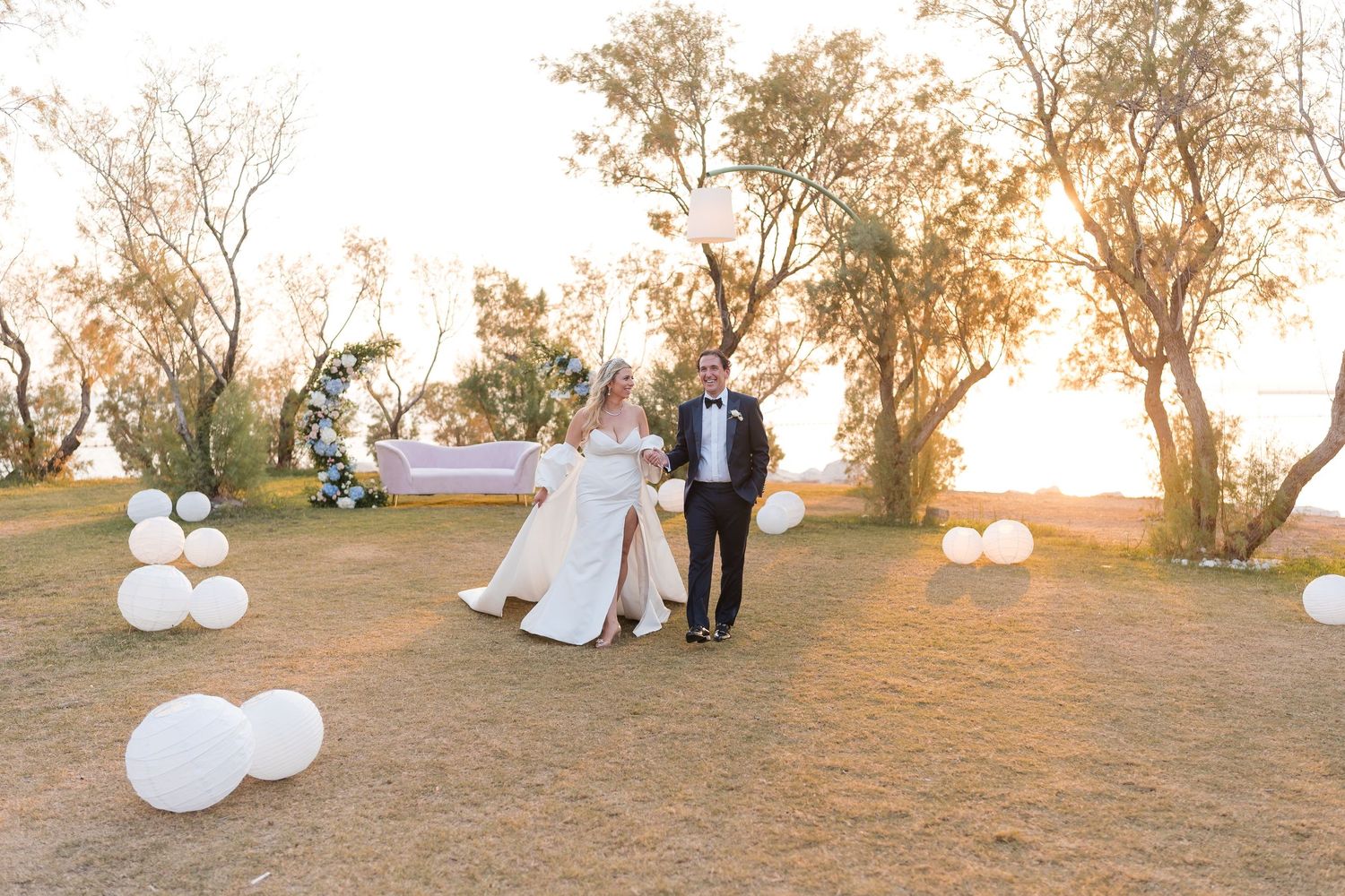 A wedding couple poses outdoors at sunset with white balloons decorating a natural landscape setting.
