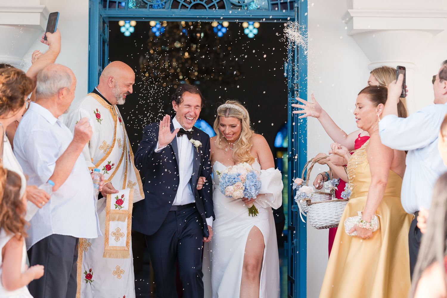 Wedding couple exits through blue doorway as guests shower them with confetti in joyful celebration.