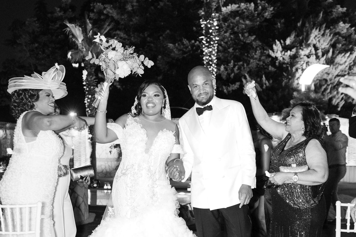 Black and white photo of a joyful bride and groom celebrating at their wedding reception with guests cheering around them.