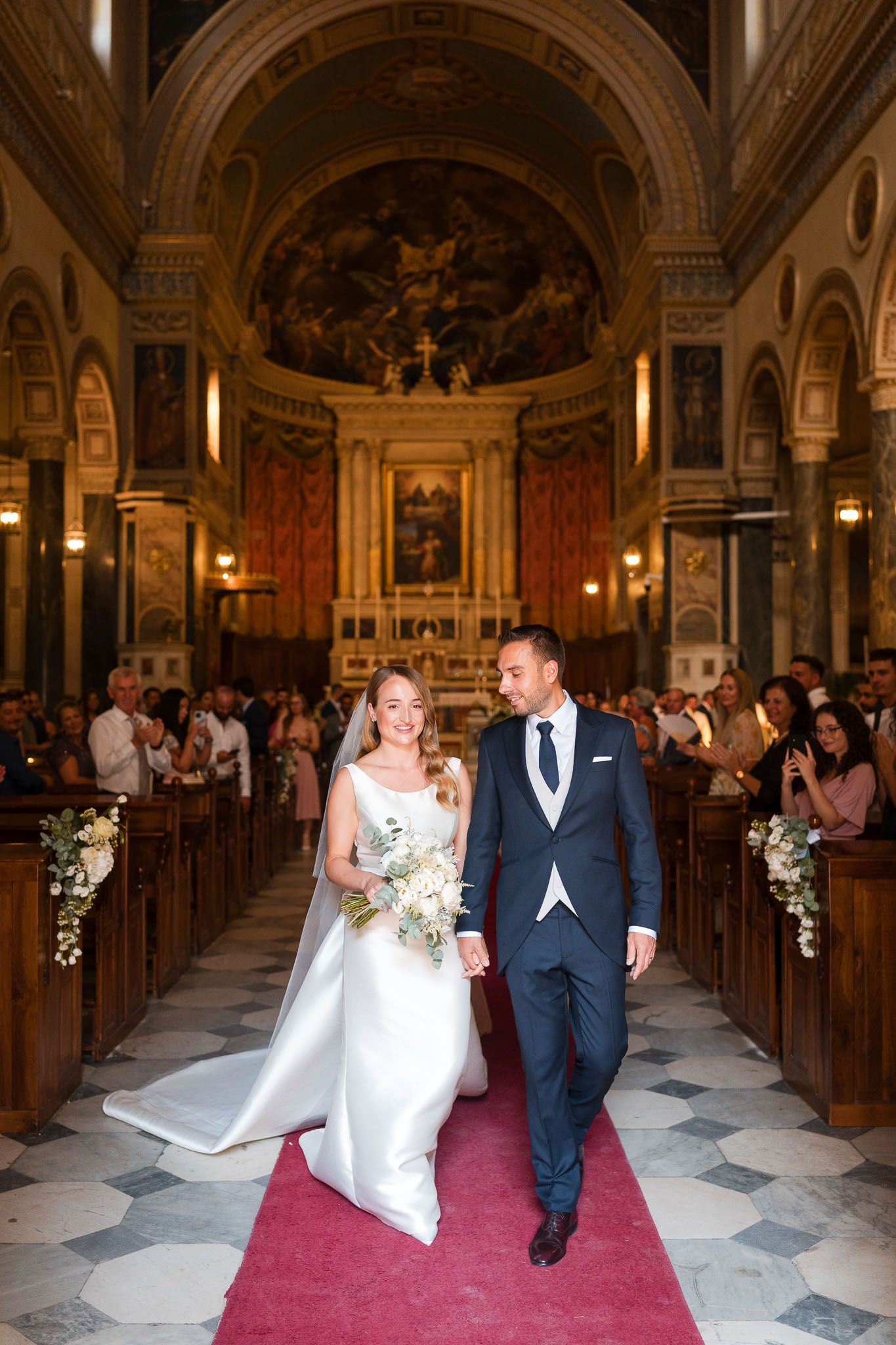 Bride and groom walk down the aisle of an ornate church after their wedding ceremony.
