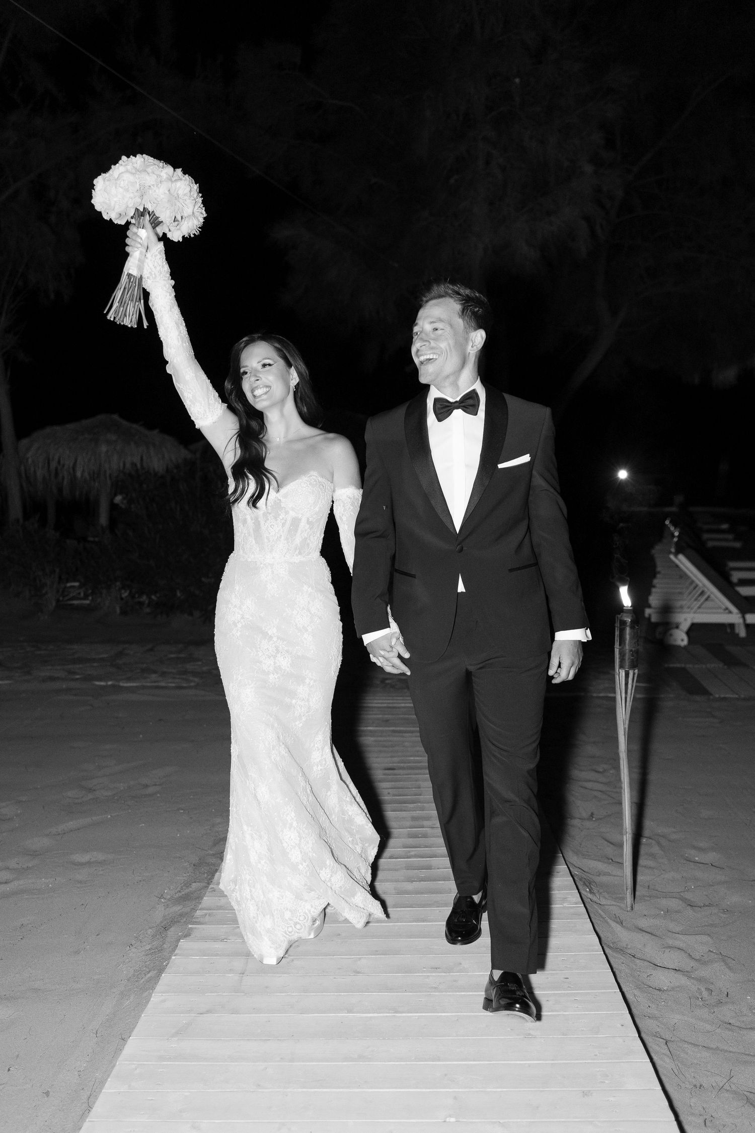 Black and white photo of newlyweds walking triumphantly at night reception.