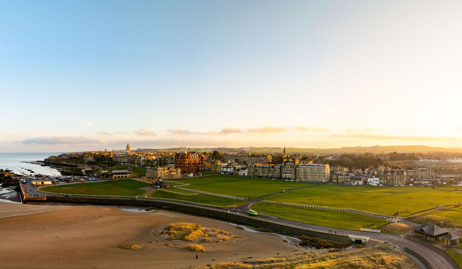 Aerial golden hour view of a seaside town with green golf fairways and sandy beach in the foreground.