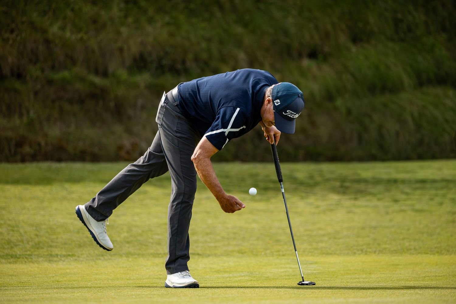 Golfer bends down to retrieve a ball from the hole on a lush green putting surface during a round.