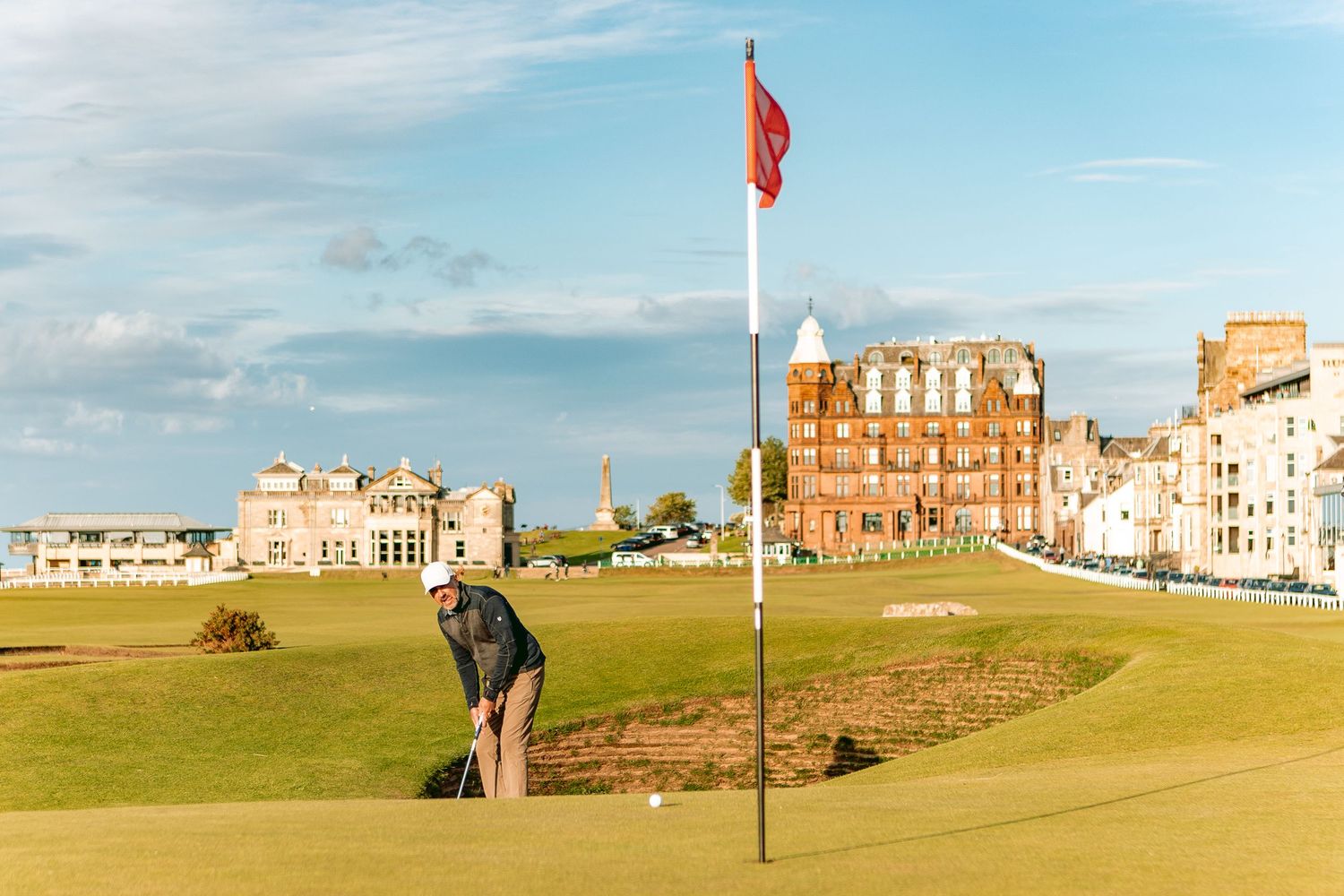 A view of a coastal golf course with green fairways and historic buildings along the shoreline.