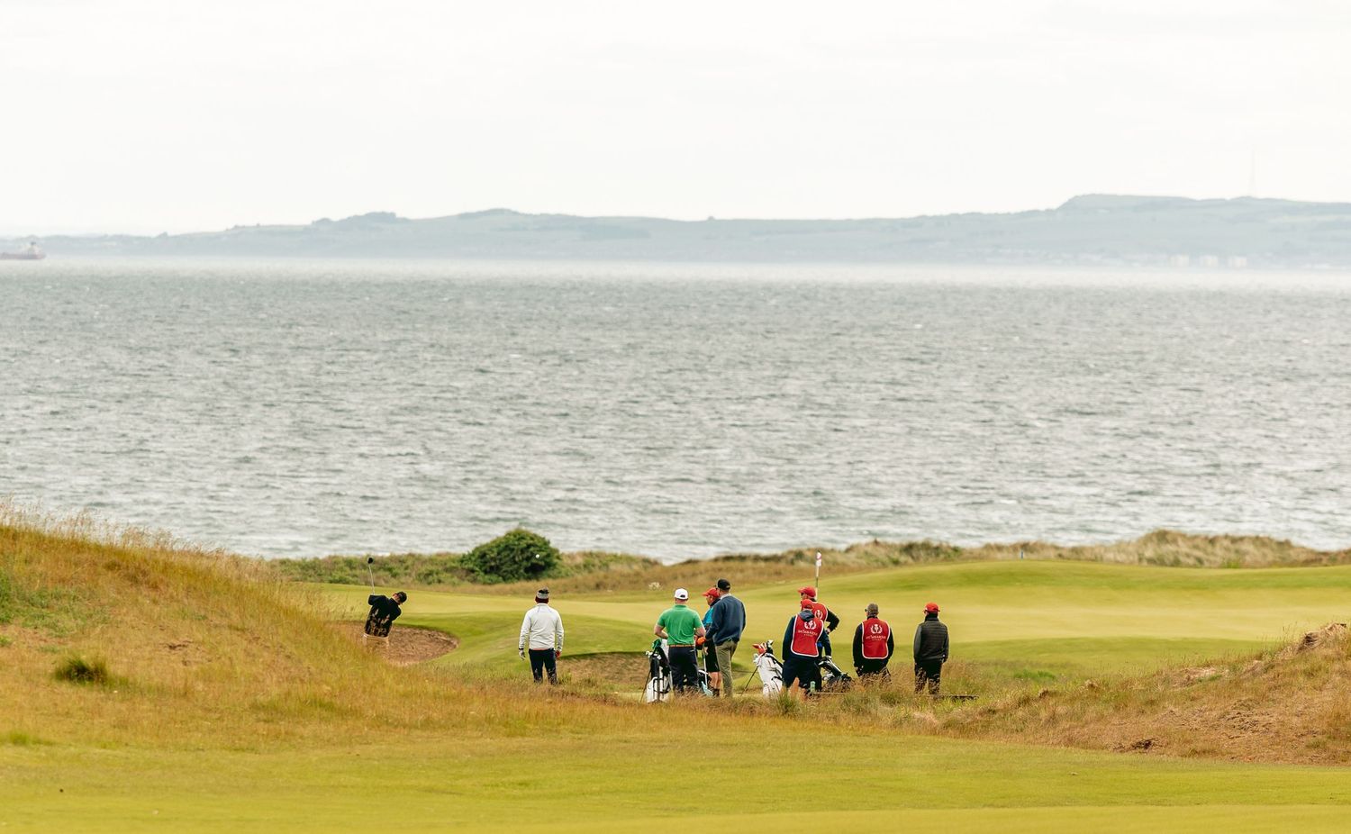 Golfers playing golf course, Dumbarnie Links, with rolling hills and ocean view.
