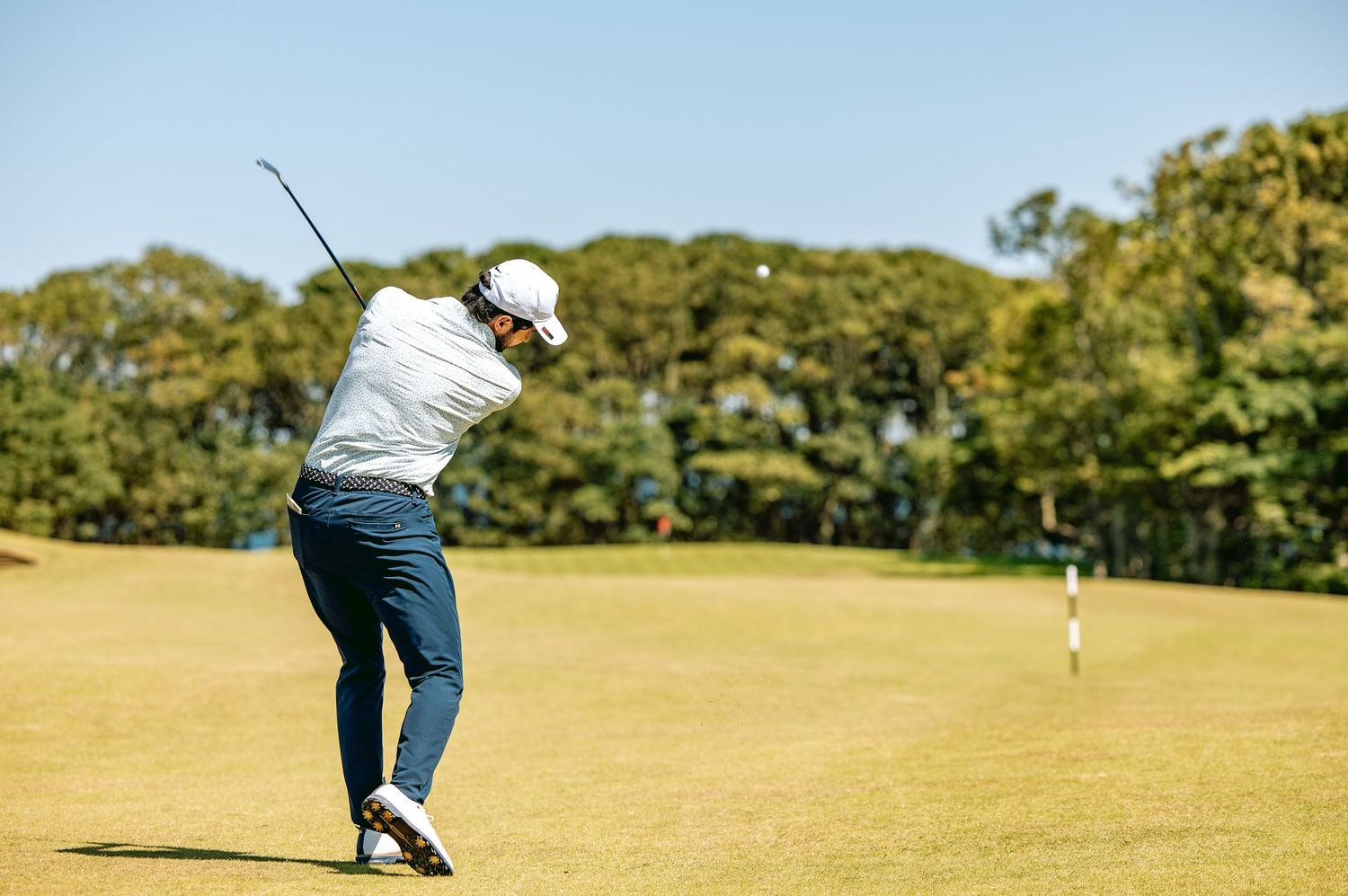 Golfer in blue pants playing a calculated shot through the line on sunny day at Kingsbarns Links.