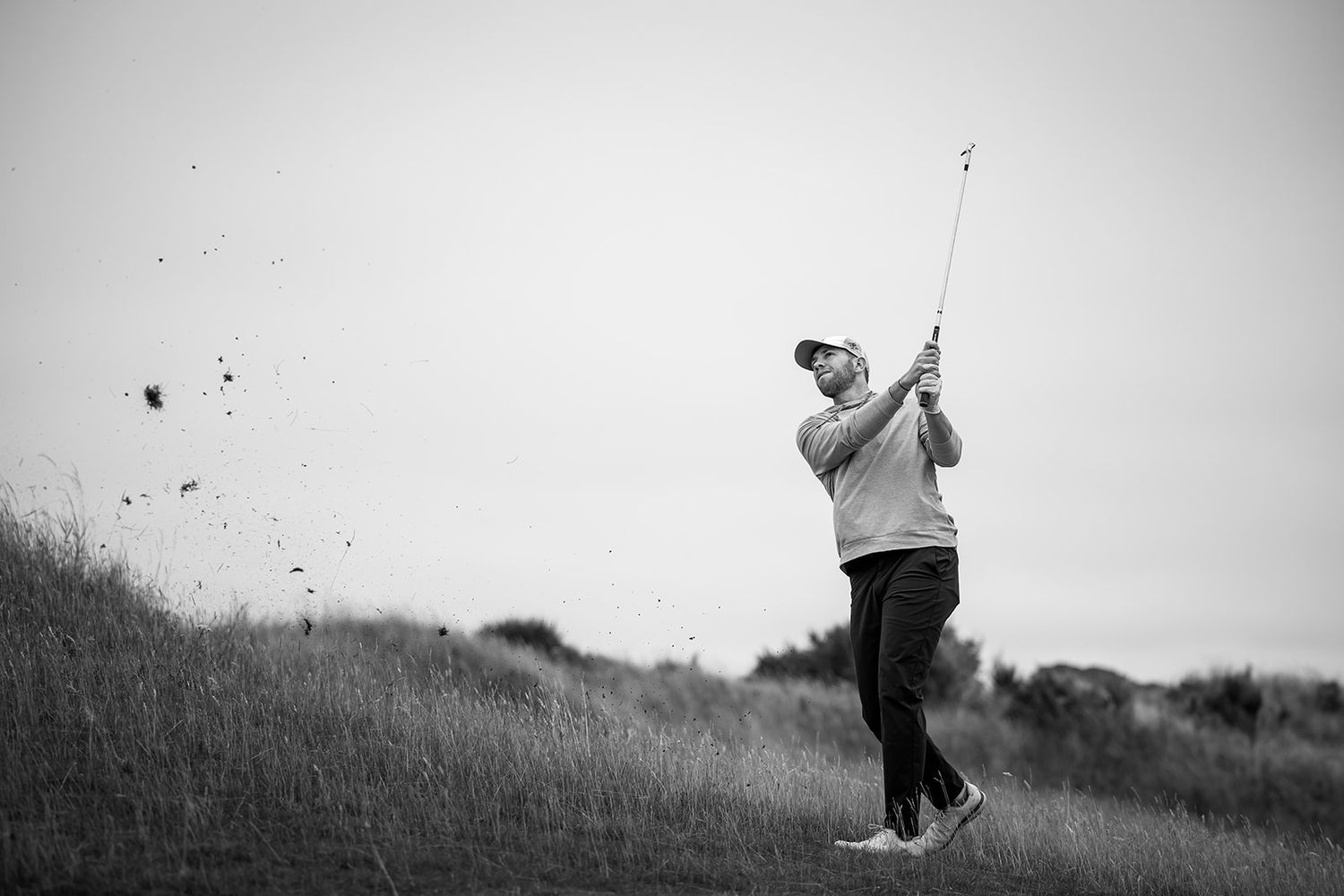 A golfer takes a powerful swing at Kingsbarns golf course, in black and white photography