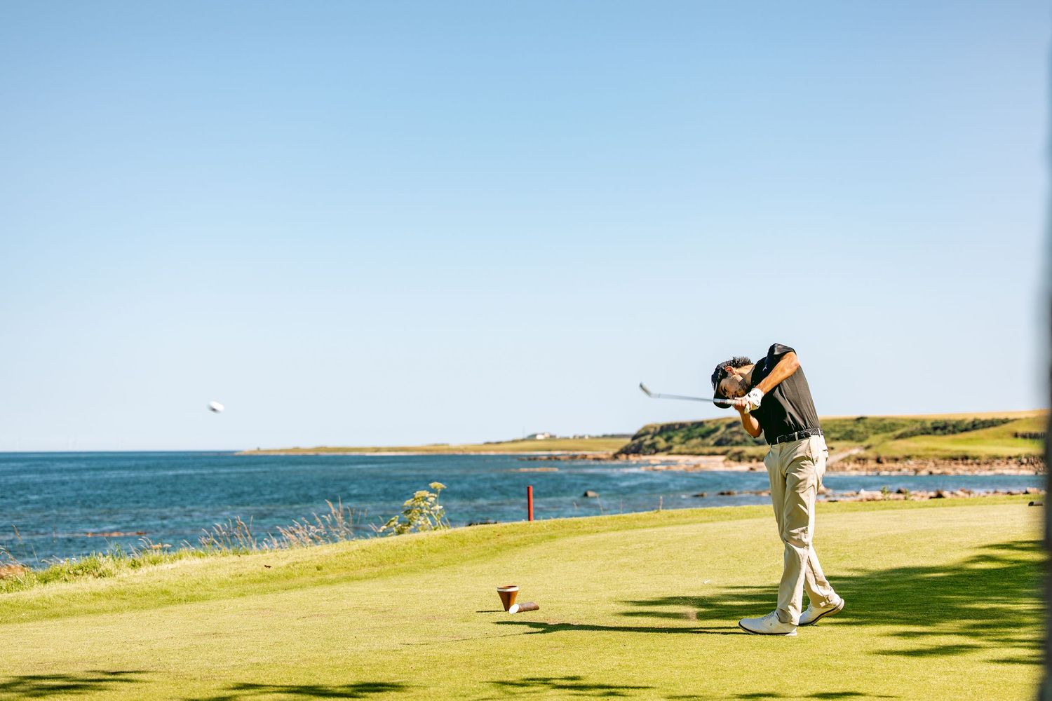 A golfer, playing at Kingsbarns Links, swinging his club after hitting the ball.