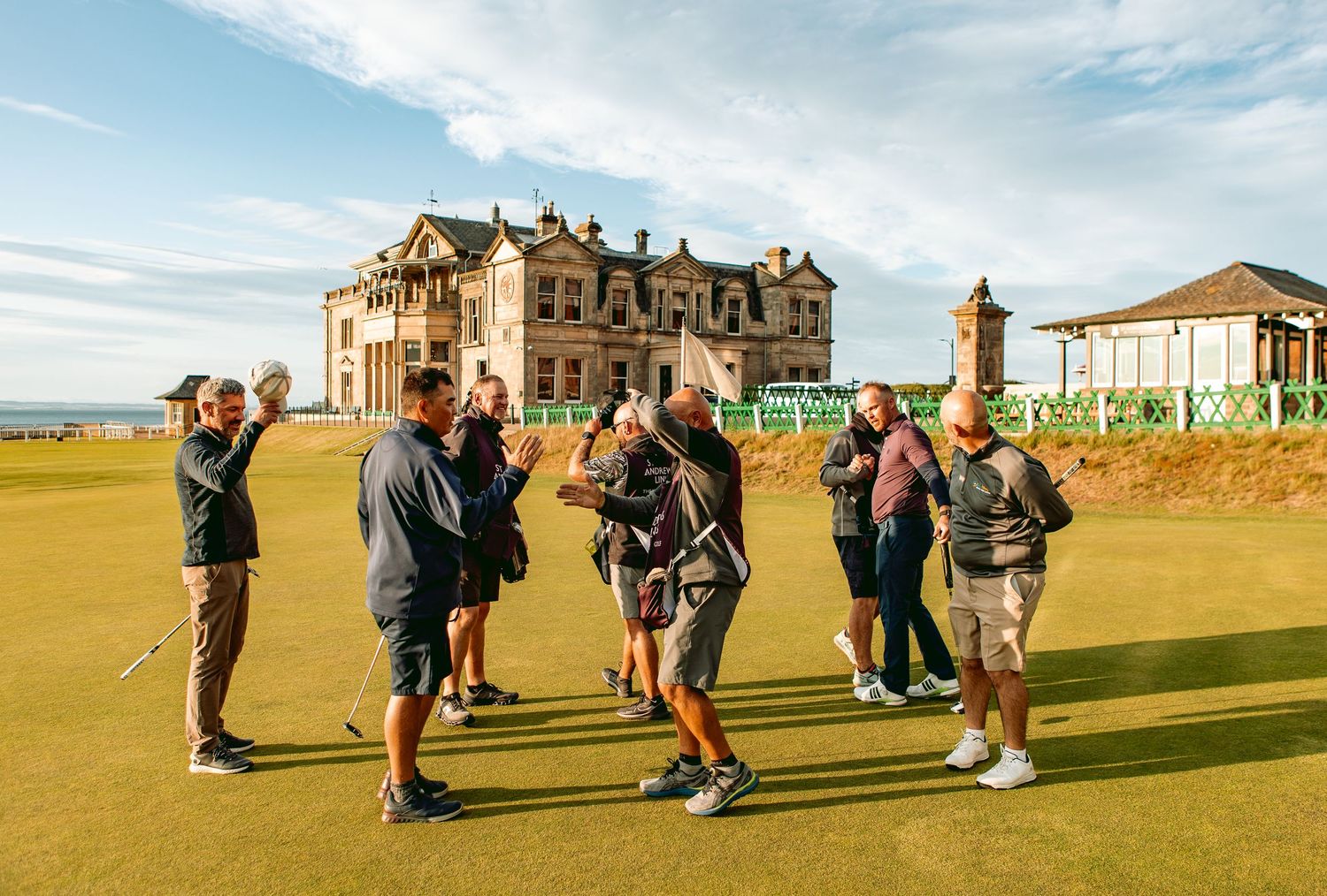 Tourists gather on the iconic St Andrews golf course with the historic Royal and Ancient Golf Club building in the background.