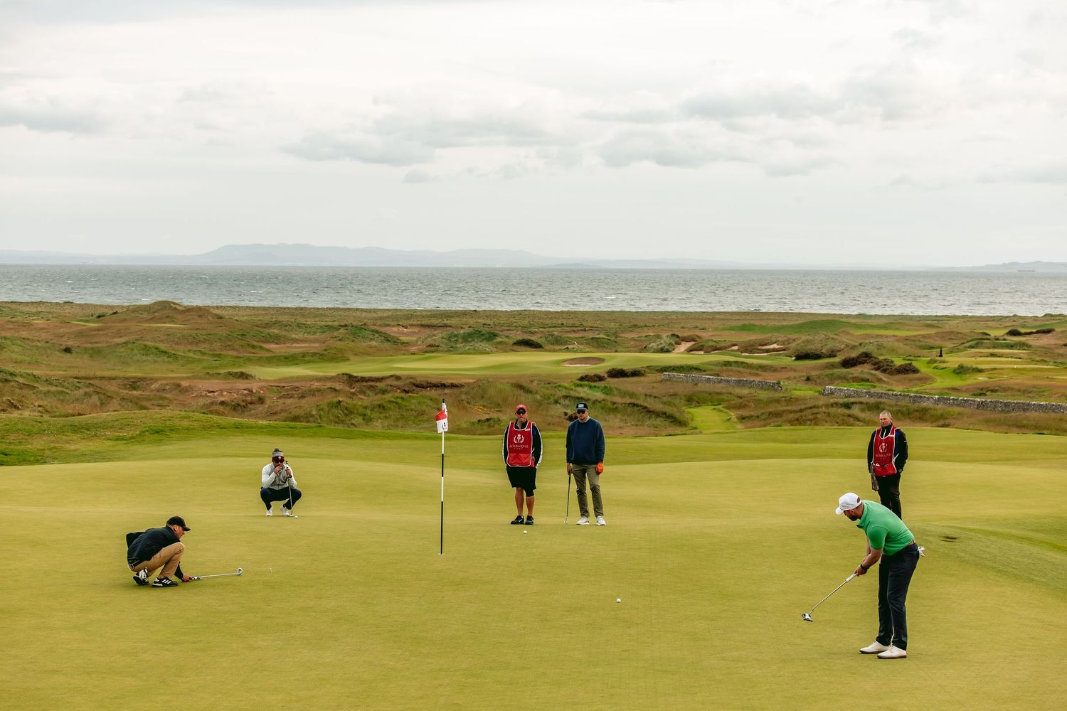 Golfers playing on the golf course, Dumbarnie Links, with rolling green fairways in the background.