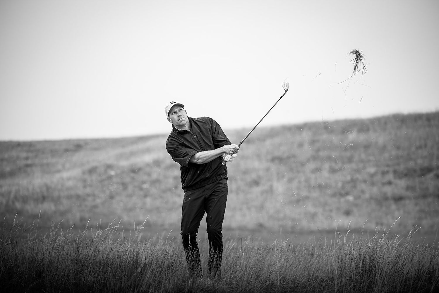 A golfer wearing cap looking far at ball after playing a shot