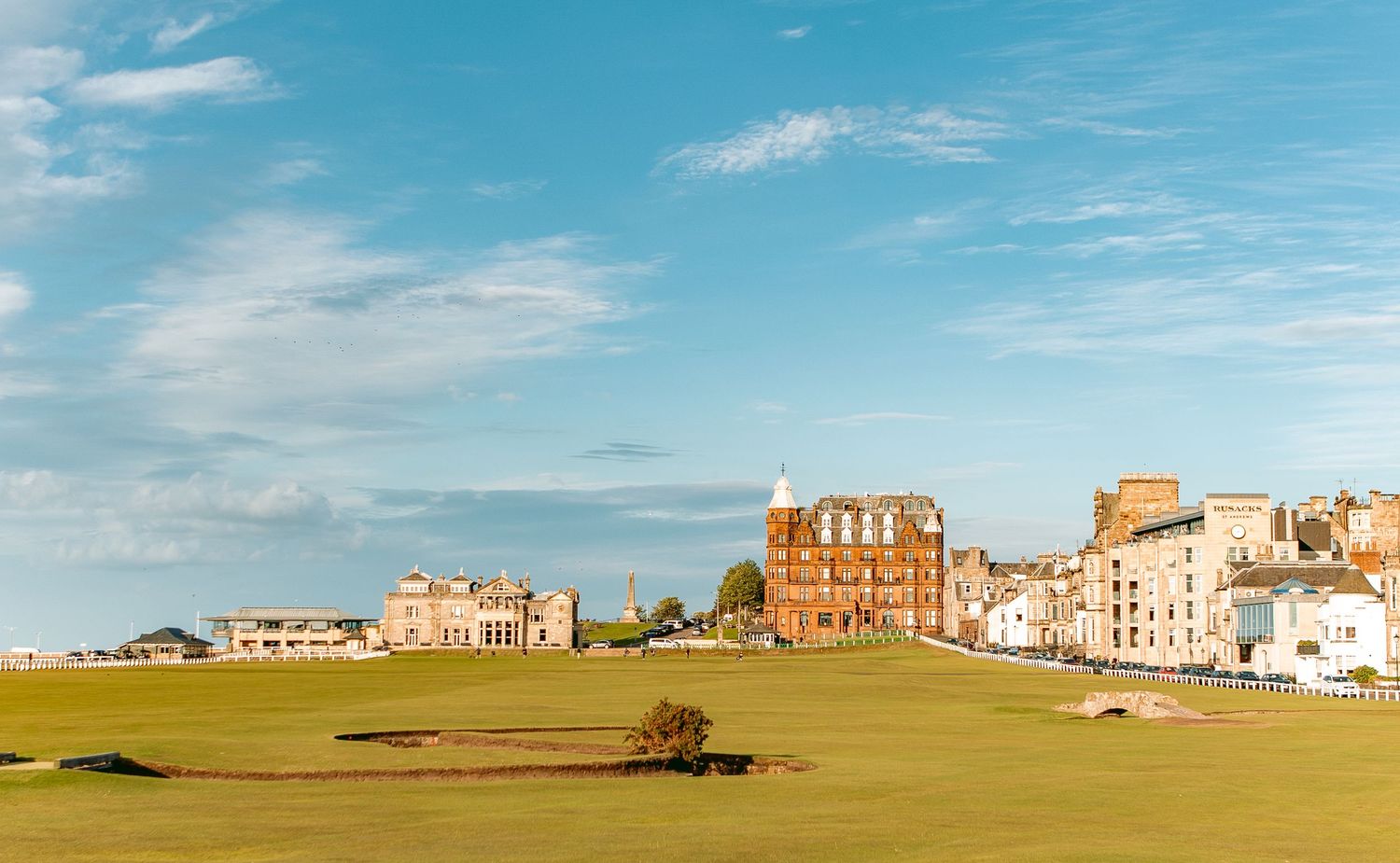 Panoramic view of St Andrews Links under a bright blue sky with scattered clouds.