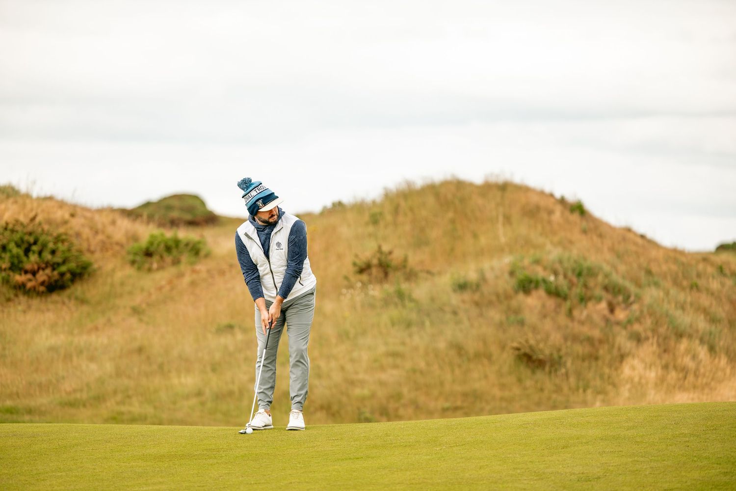 A golfer, in white gilet, is ready to play a shot.