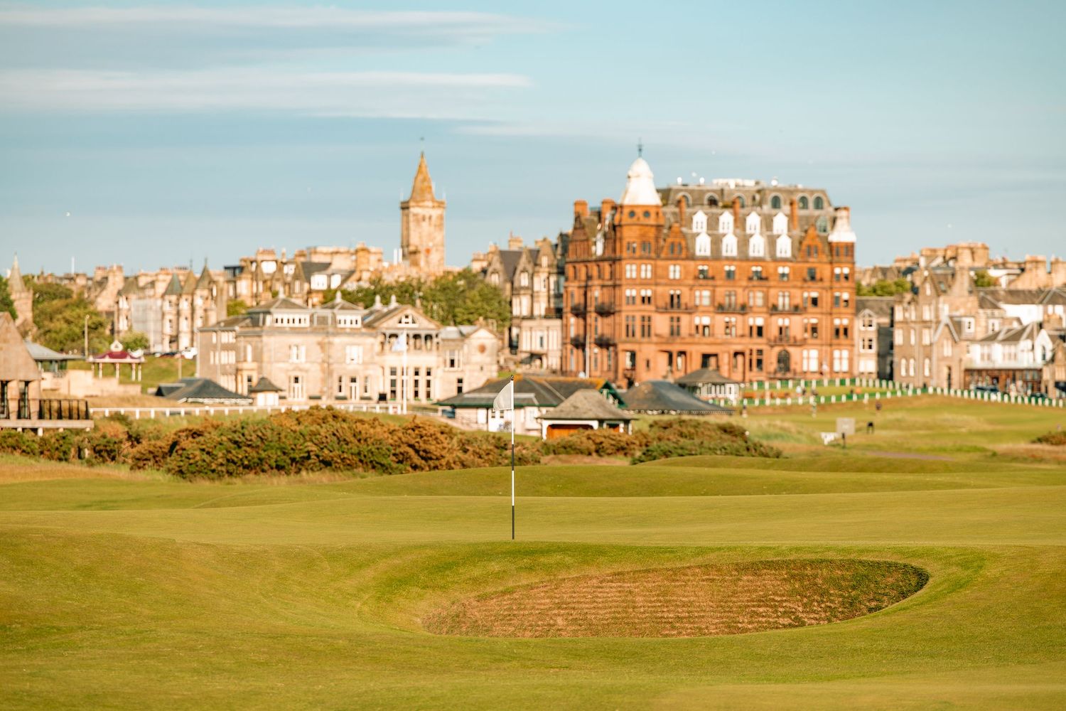 A view of the historic St Andrews golf course and clubhouse against a blue sky in Scotland.