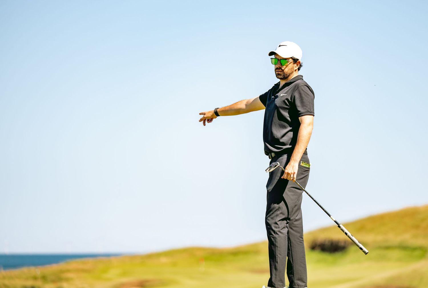 A golfer wearing white cap pointing in ball's direction.