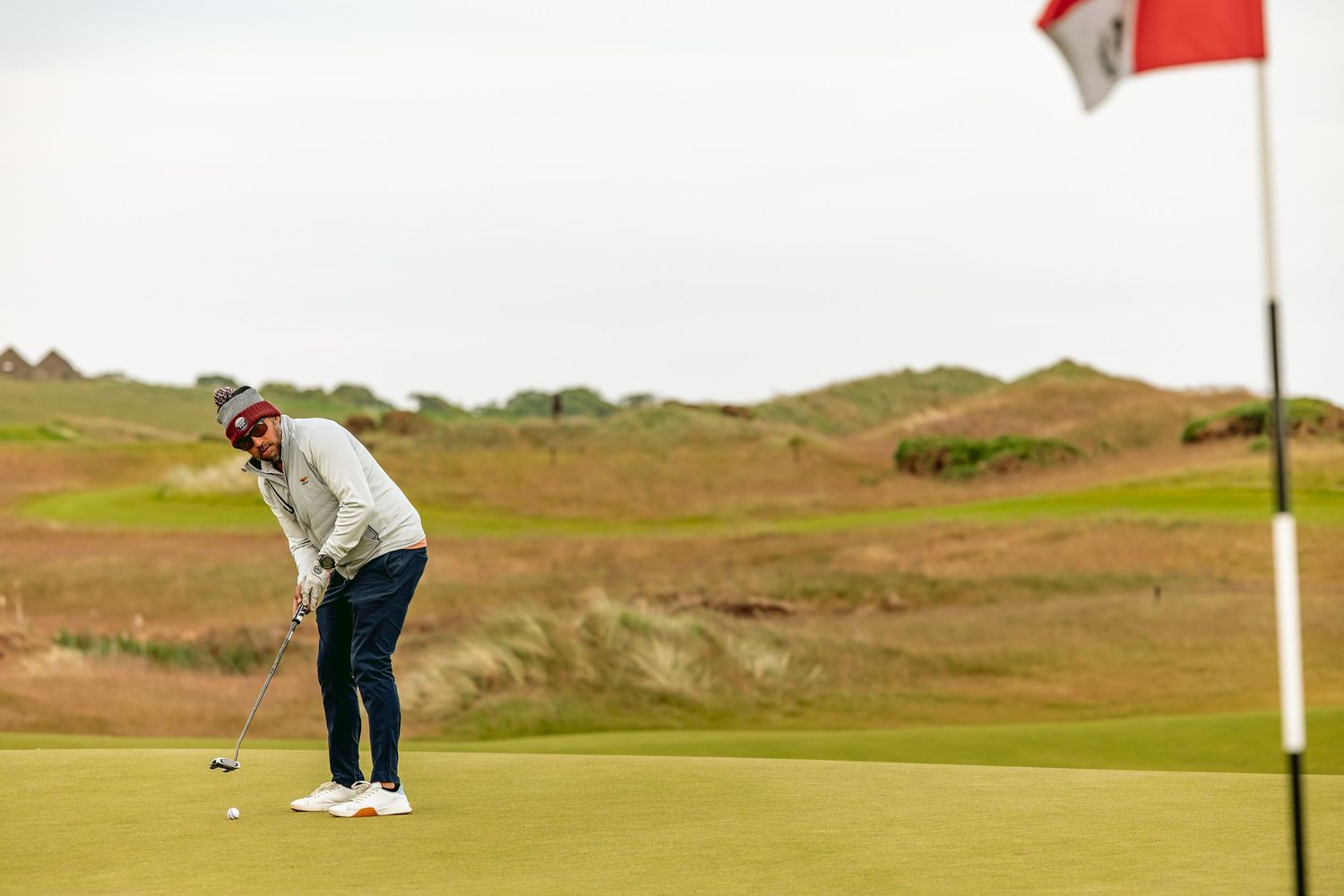 Golfer in white jacket playing at Dumbarnie Links ready to put the ball into the hole.