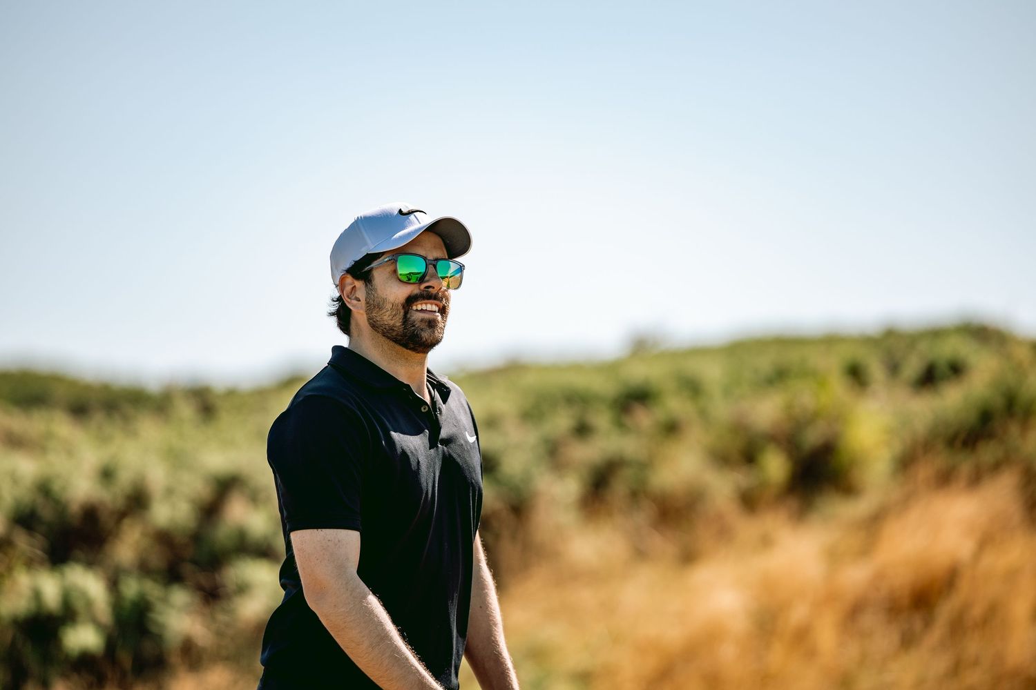 Happy man, wearing cap and stylish sunglasses, playing at Kingsbarns Links.