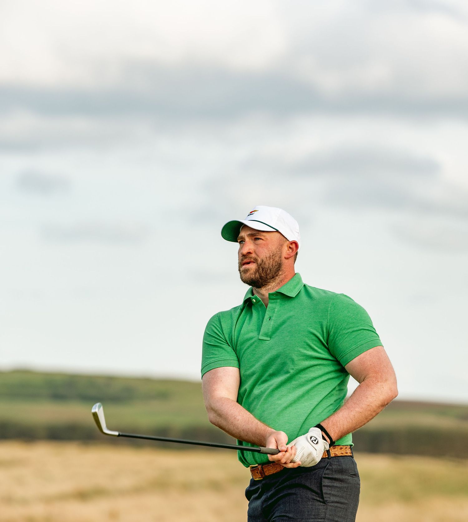 A golfer in a green shirt takes a swing with a club at Dumbarnie Links.