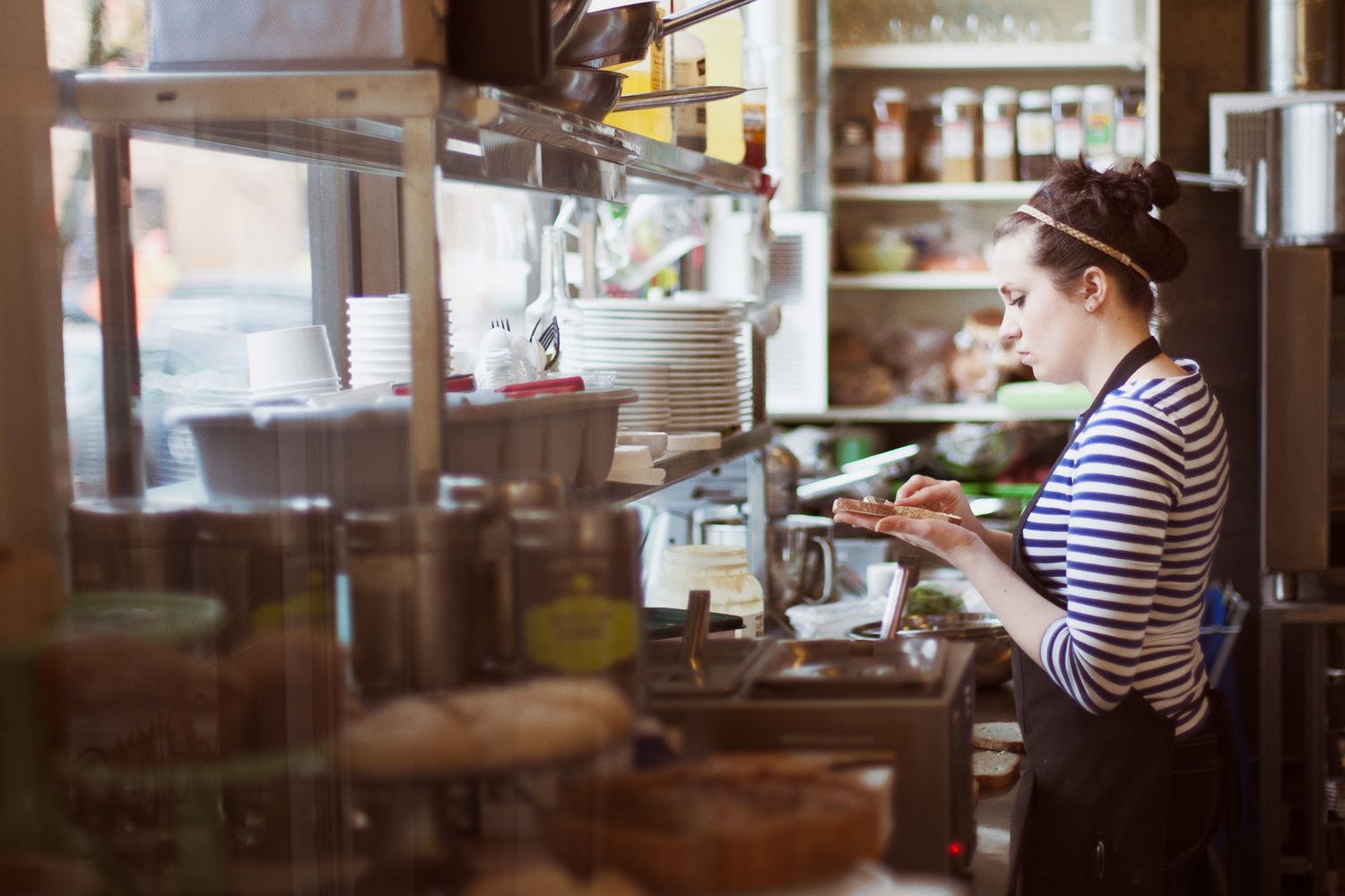 Someone in a striped shirt stands at a cafe counter and prepares a sandwich.