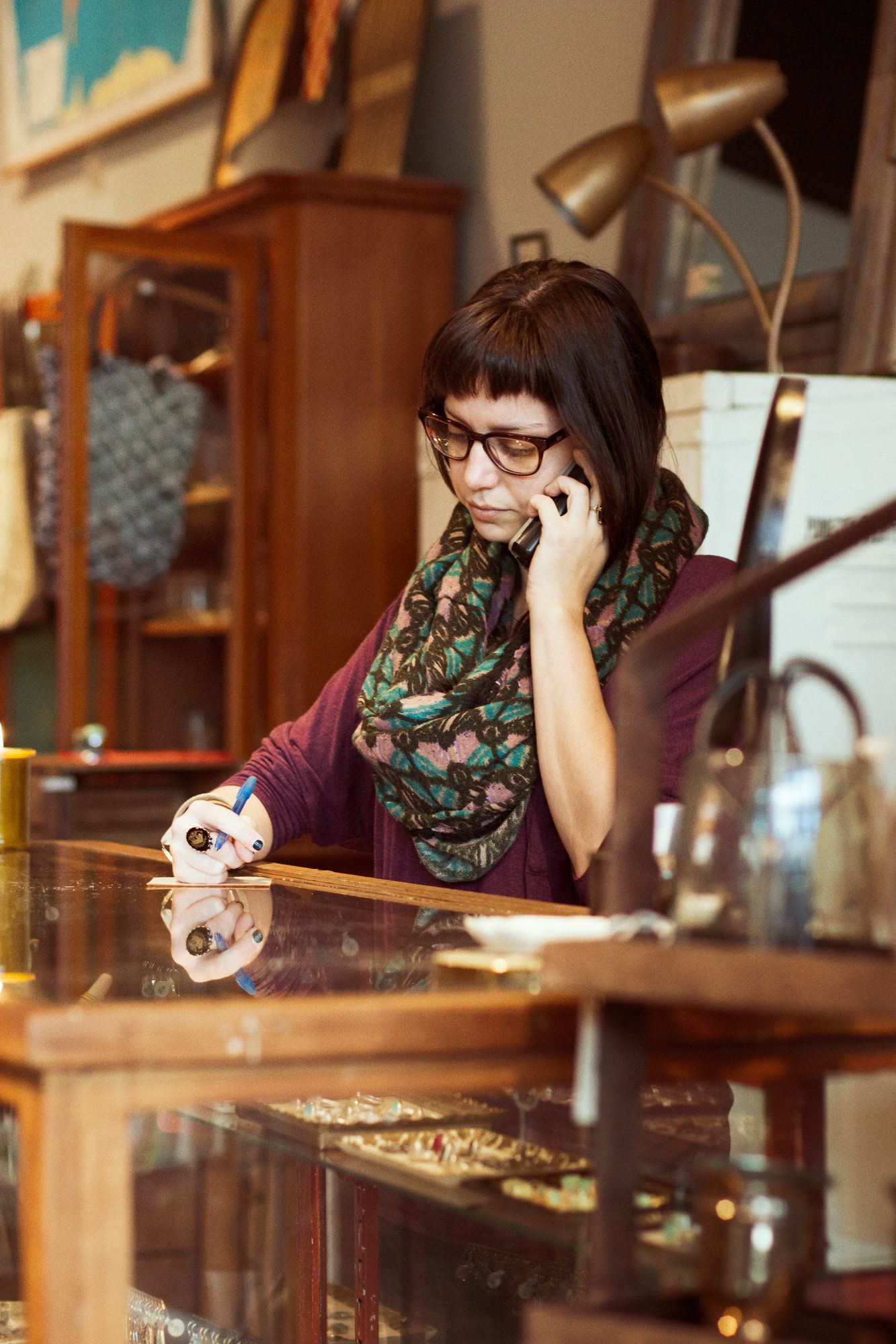 An employee is sitting down and on the phone with someone. They are taking notes with a pen and paper while listening to what's being said.