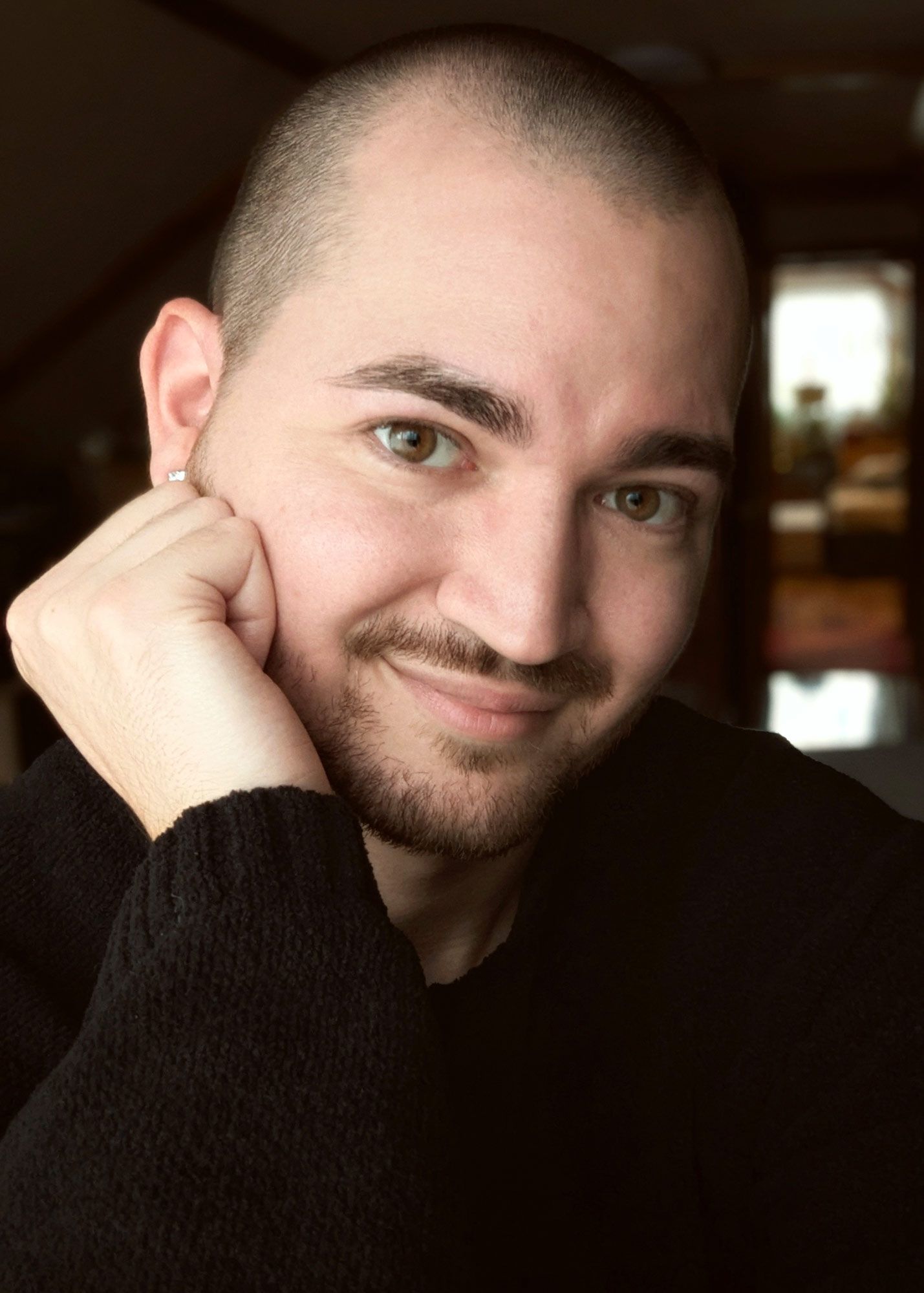 Portrait photograph of someone looking toward the camera and smiling slightly as he rests his head on his hand.