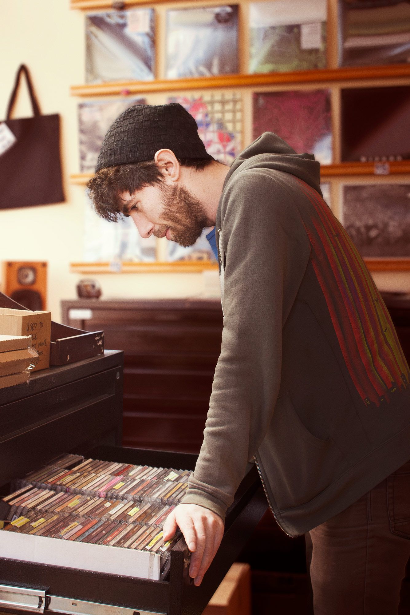 An employee at a record store rests his hands at the edge of an open drawer full of cassette tapes as he looks over the contents.