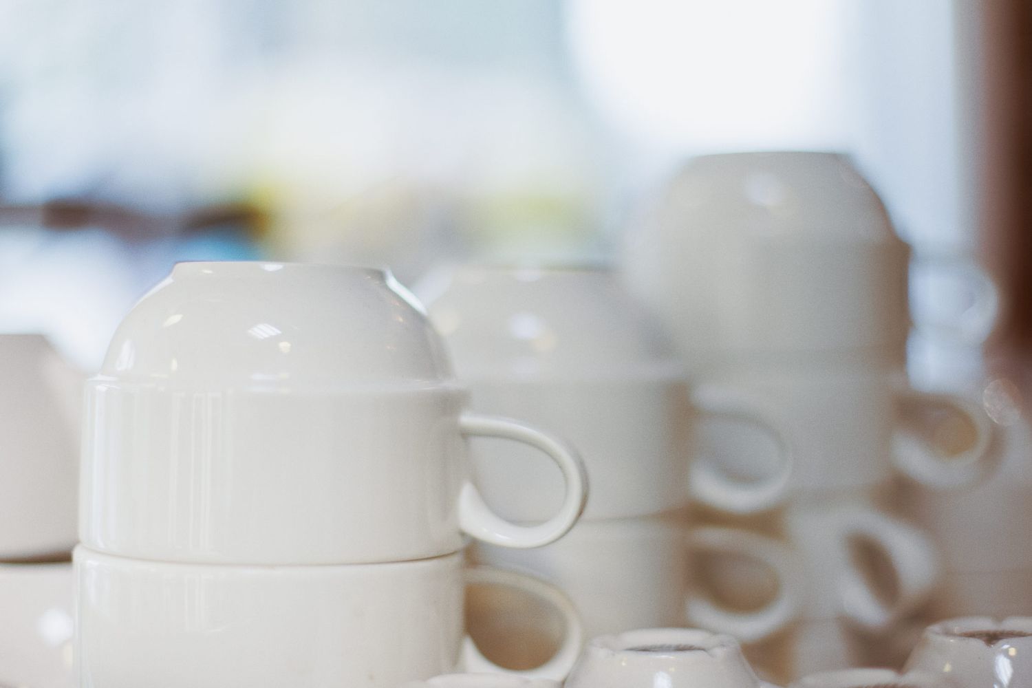 A row of white ceramic coffee cups lined up on a counter with soft blurred background lighting.