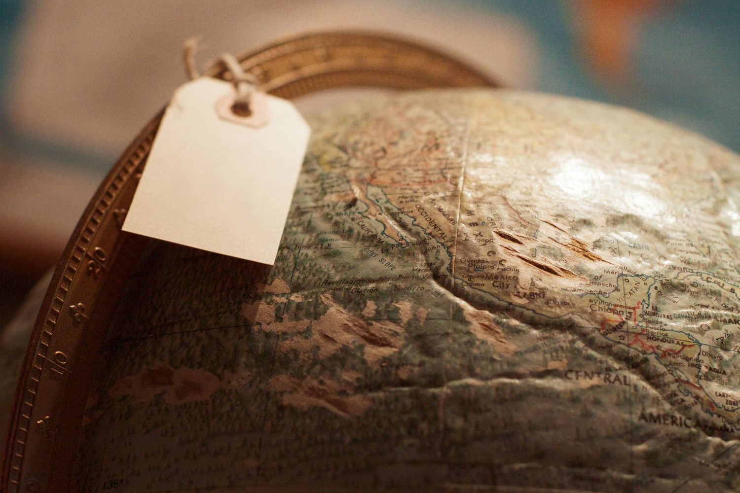 An old globe of the world fills the frame. A hanging tag rests on top, attached to the metal meridian.