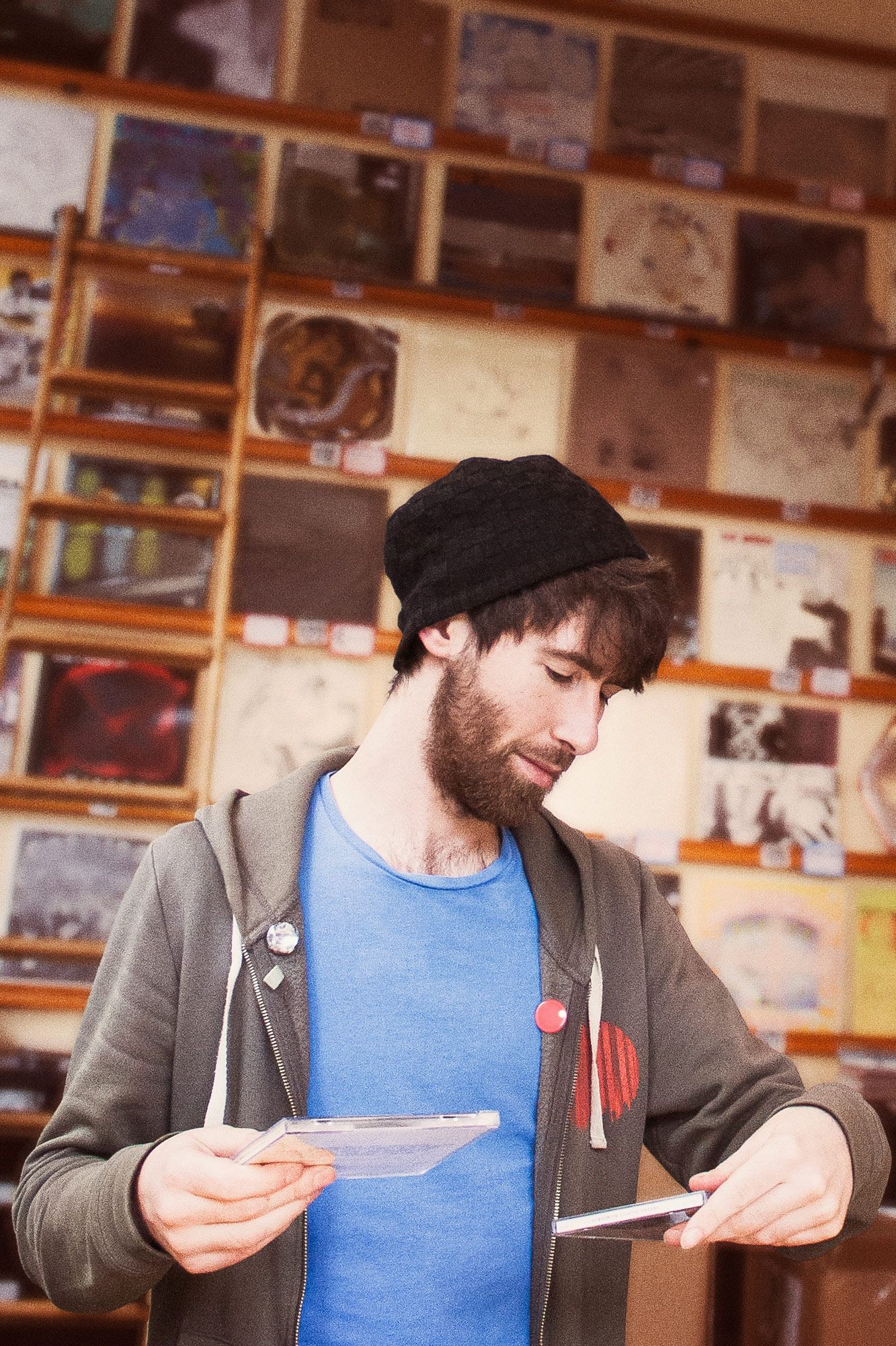 A record shop employee looking down at two CD albums in each hand. A wall of records fills the background.