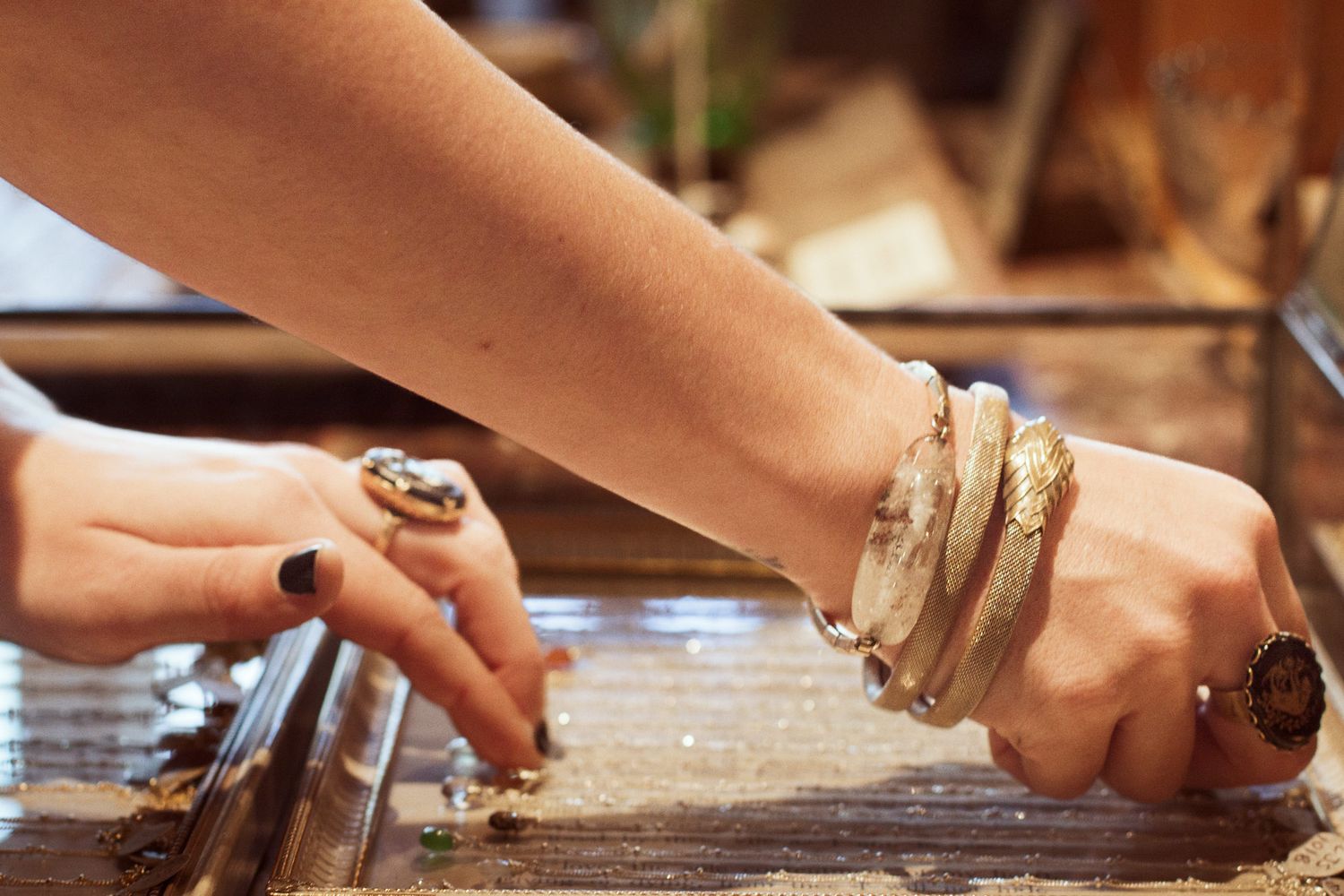 Someone wearing bracelets and rings is neatly setting a necklace into a display box, making sure that the chain is straight and well placed.