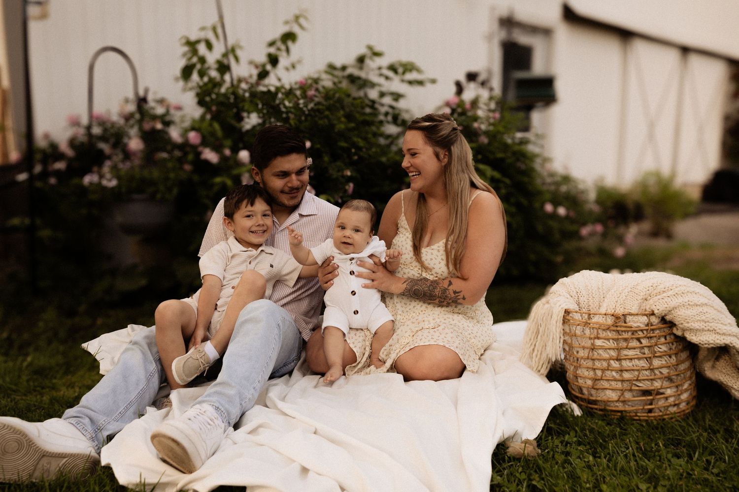 Happy family lounging together on white blankets outdoors during a cozy photoshoot session.