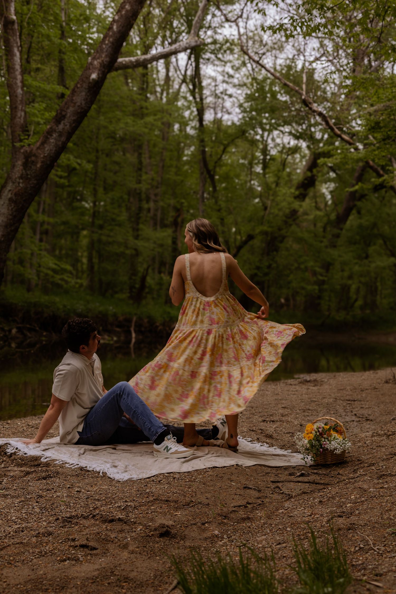 Couple lounging on blankets in a wooded area as dress fabric flows in the breeze.