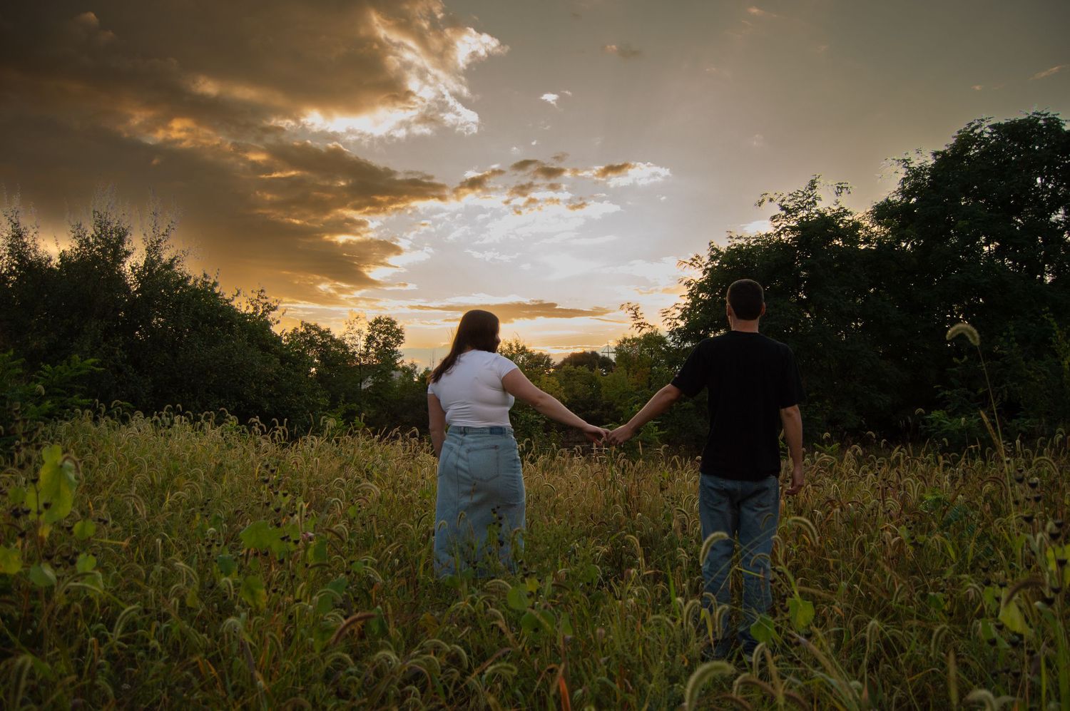 A couple holds hands while walking through a field at golden hour.