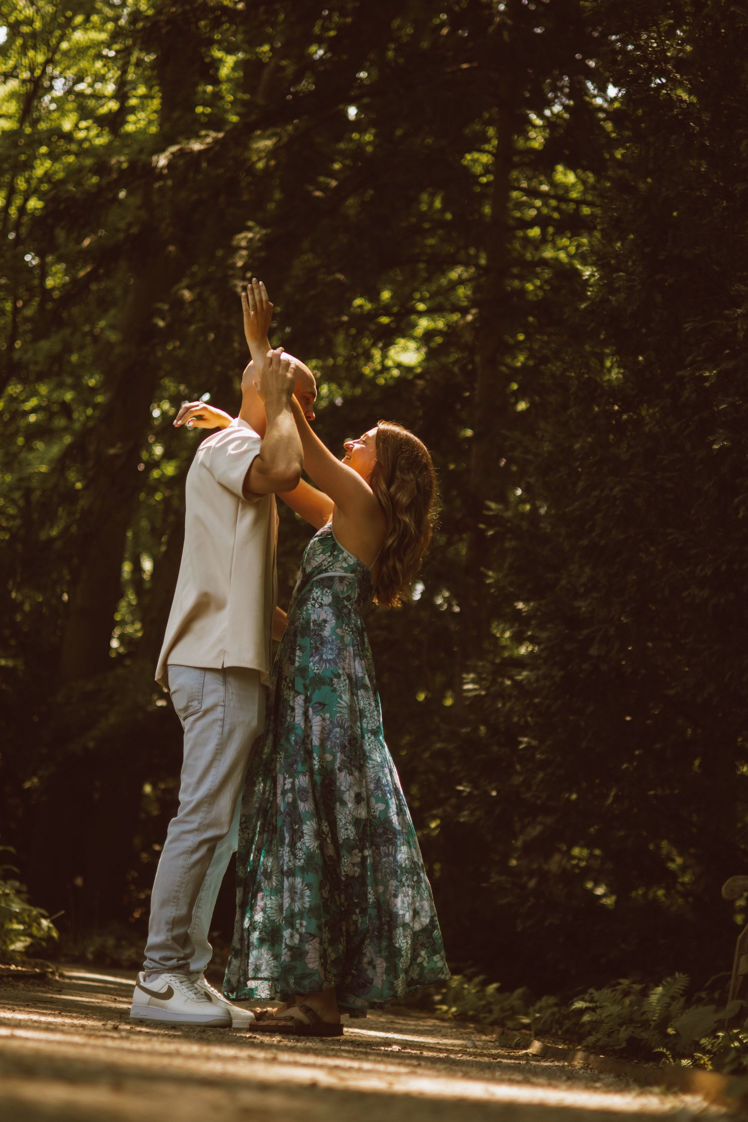 Two people share an intimate dance moment on a sunlit forest path.