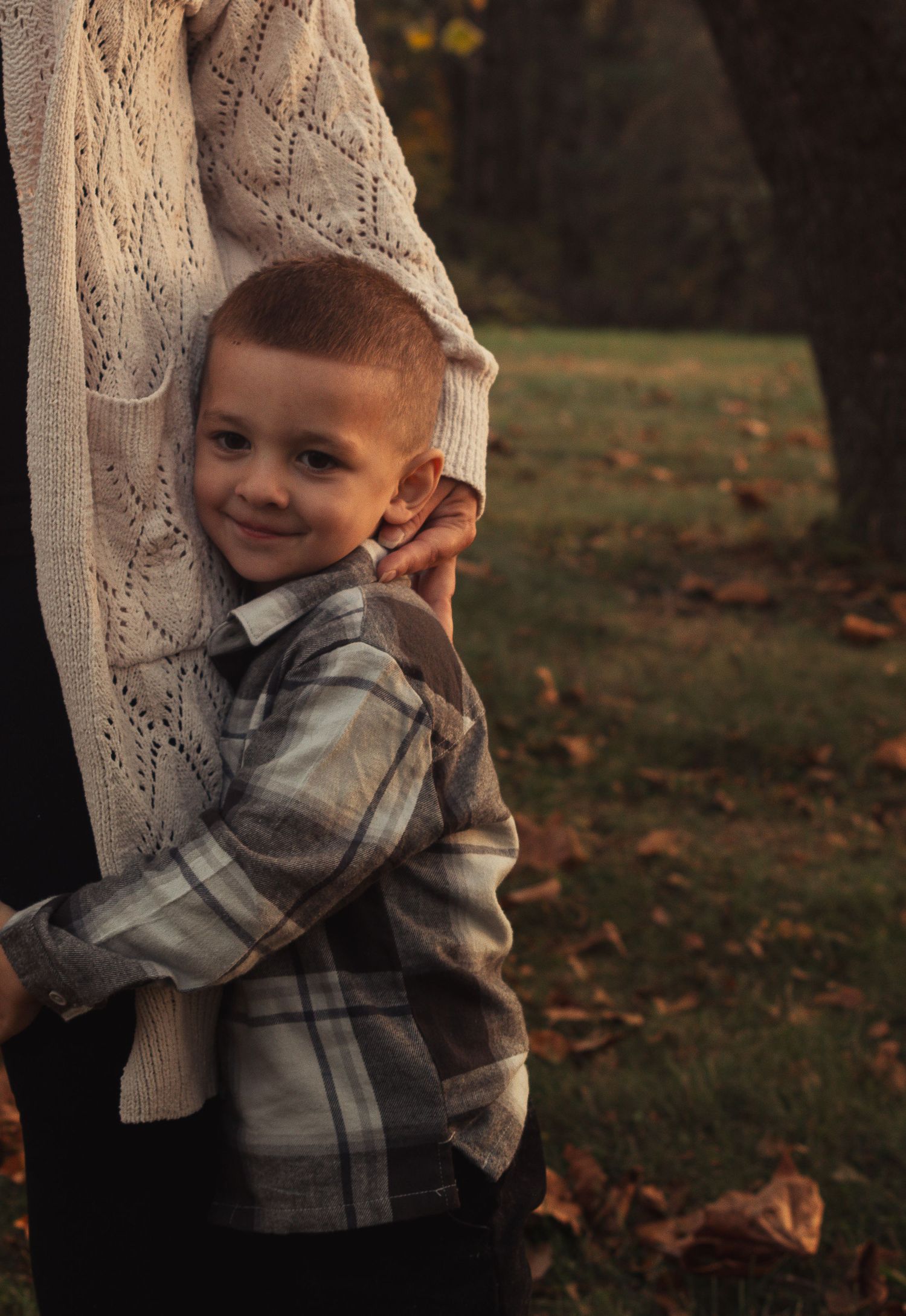 Child in plaid shirt smiling outdoors during golden hour in an autumn setting.
