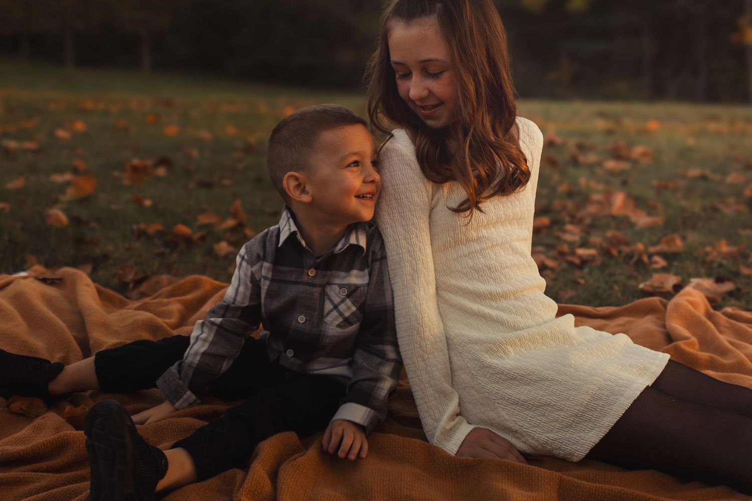 Family lounging on ground during fall photoshoot with warm sunset lighting.