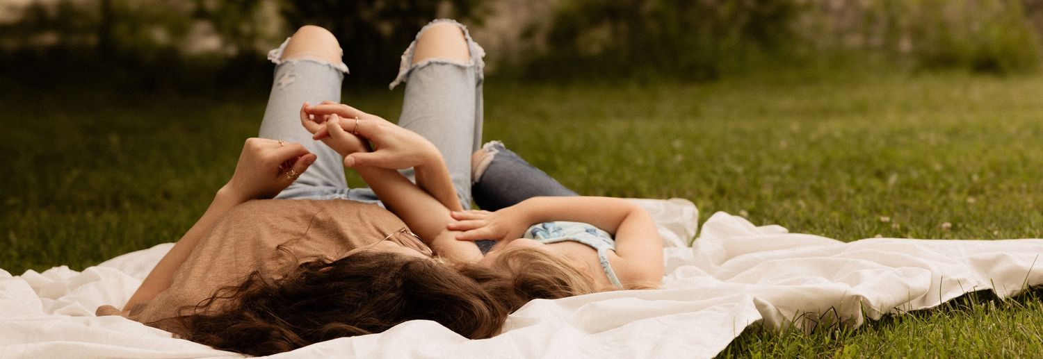 Couple lying on white blanket in grass during outdoor photo session.