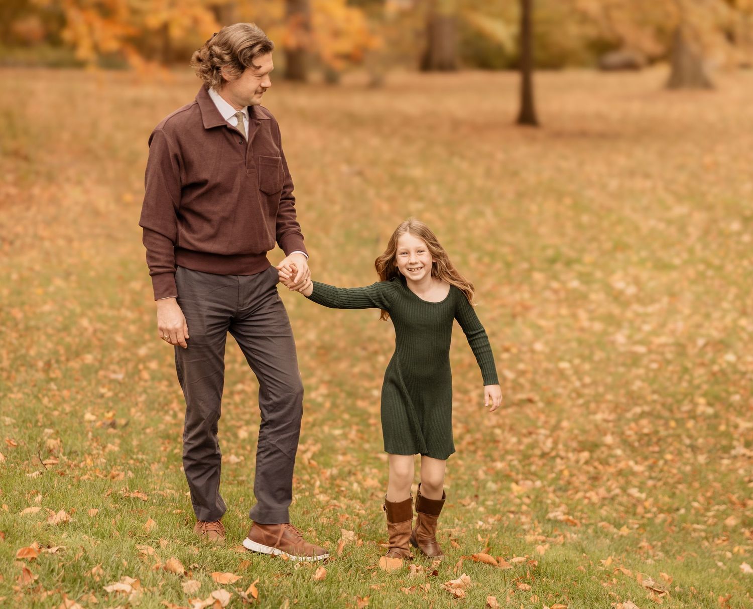 People walk and play together on a path covered in golden autumn leaves during a fall photo session.