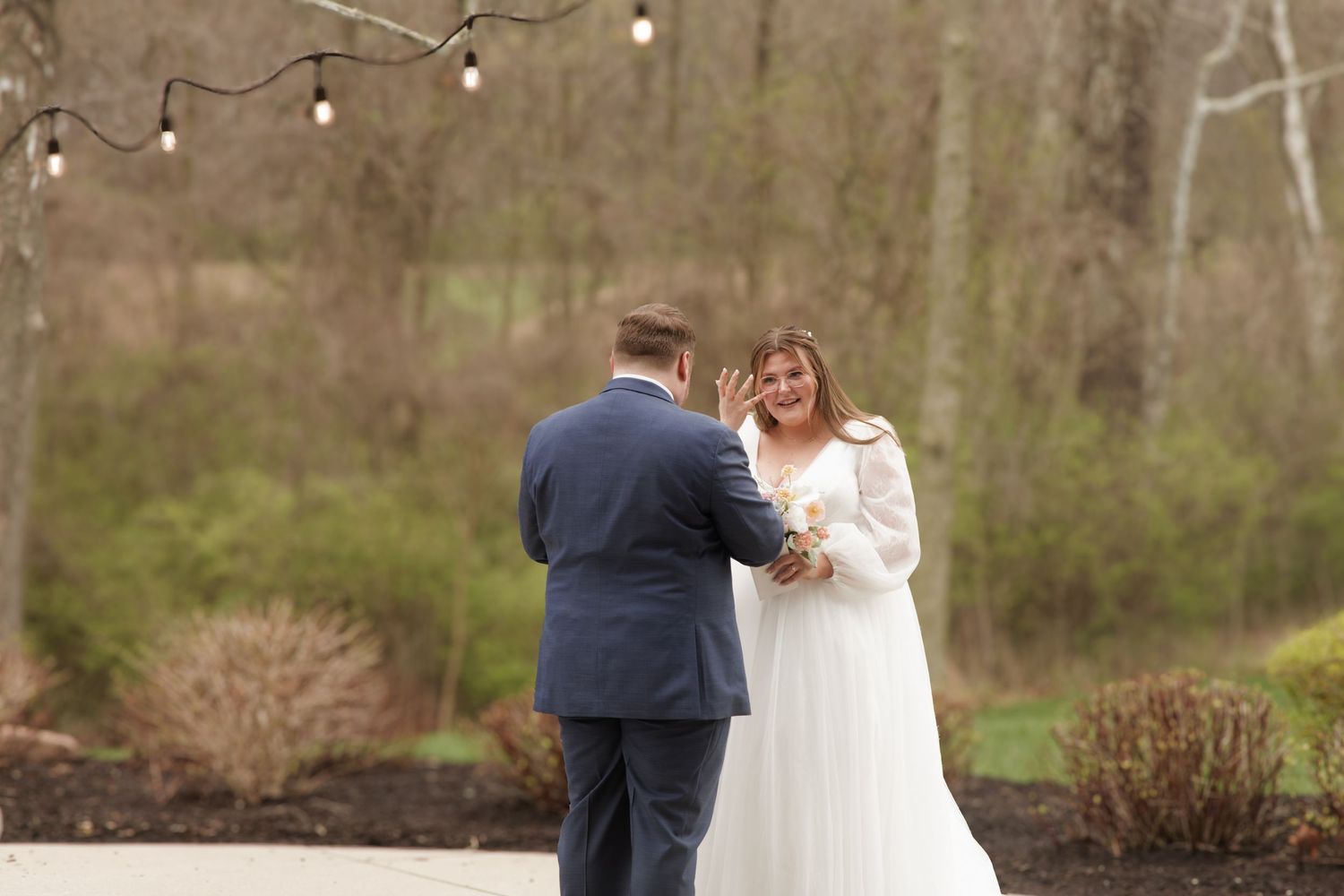 Bride and groom share a tender moment outdoors with string lights in the background.
