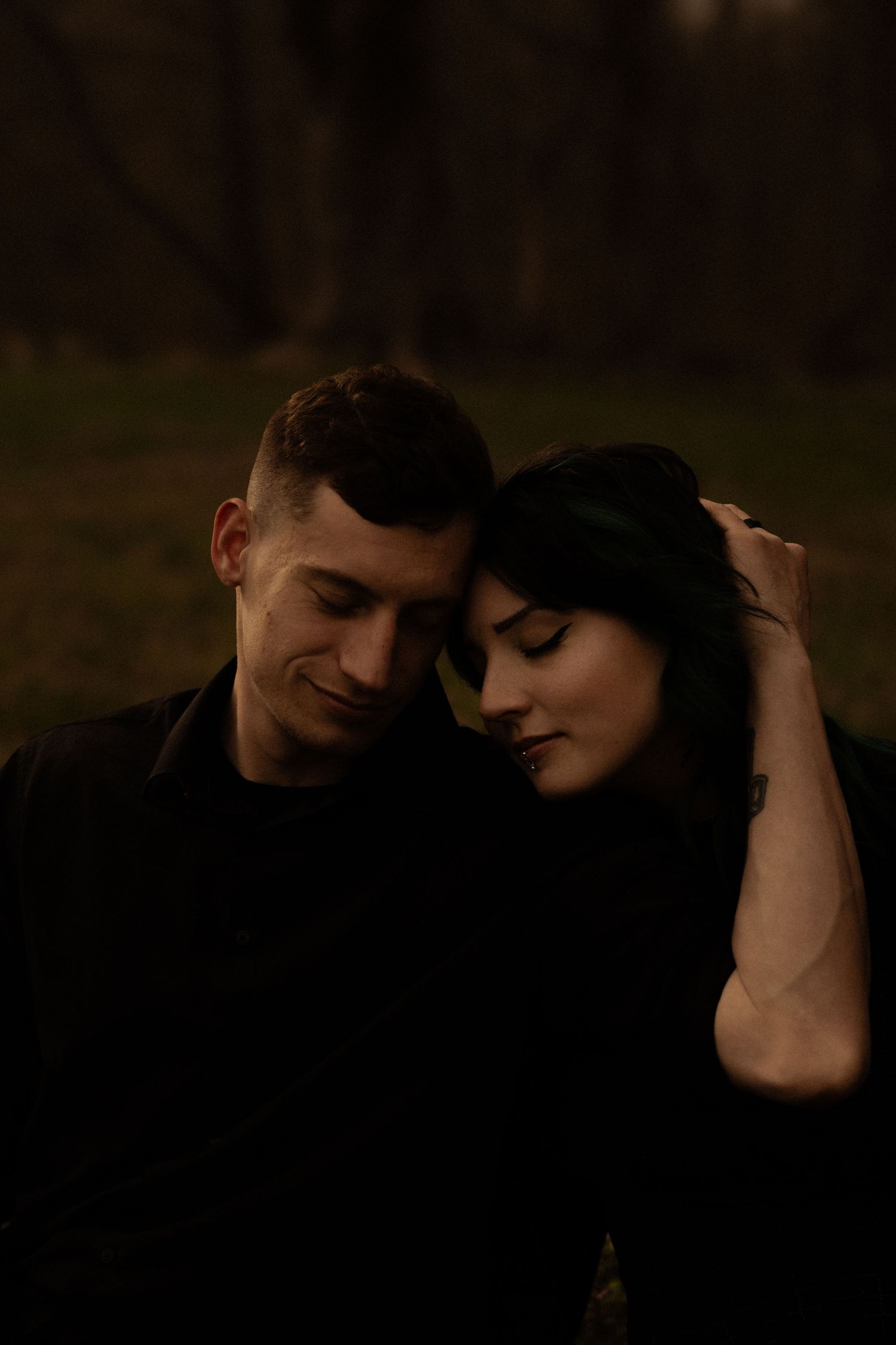 Two figures in dark clothing share an embrace in a moody, atmospheric outdoor setting.