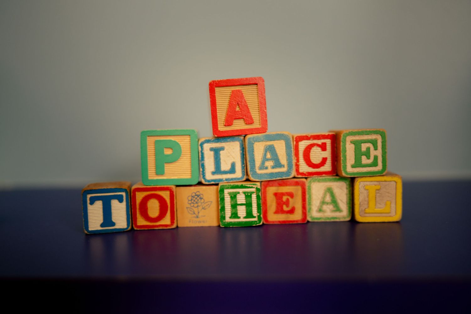 Colorful wooden alphabet blocks stacked to spell A Place To Heal on a purple surface.
