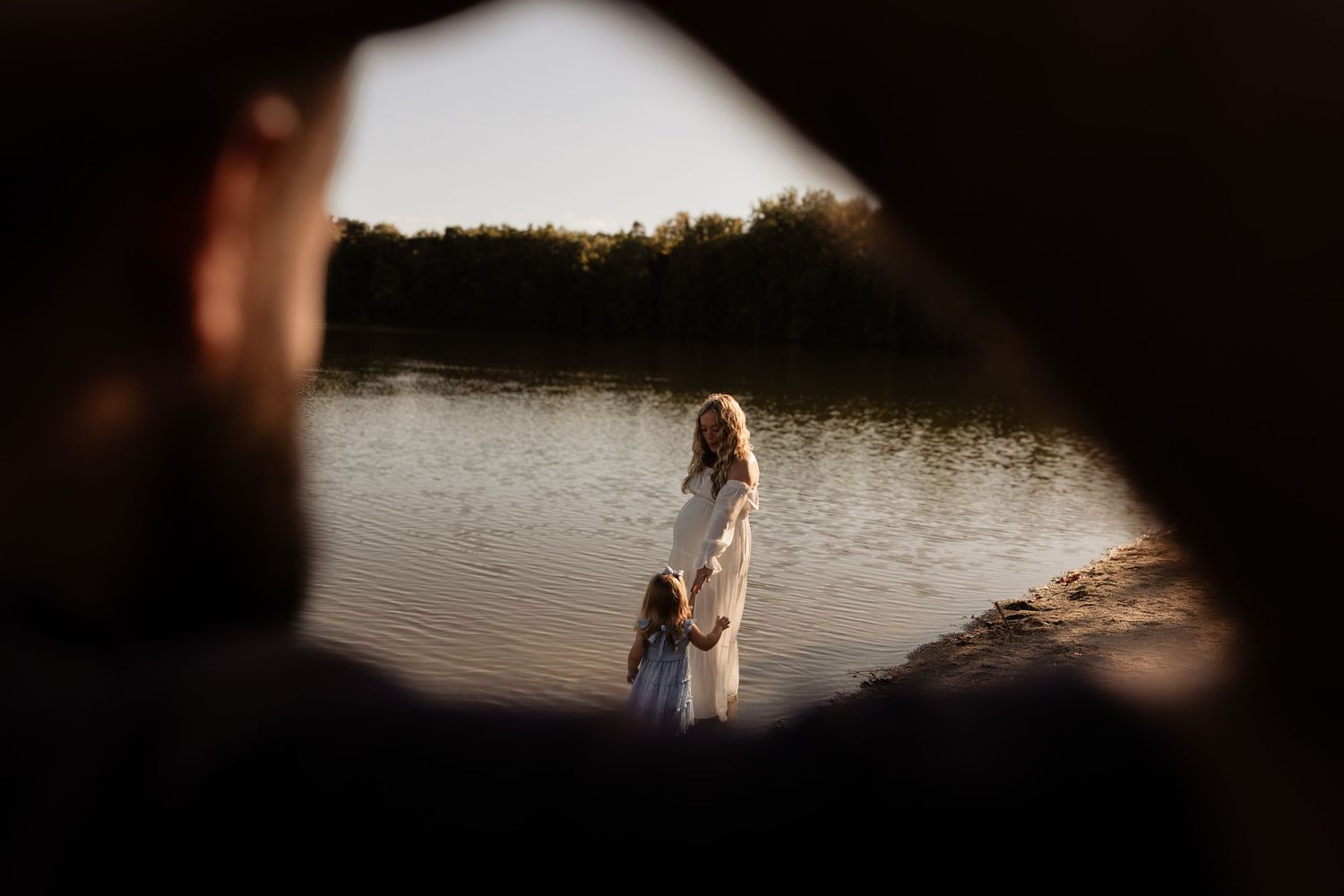 A romantic couple stands silhouetted at sunset by a serene lake creating a beautiful engagement photo moment.
