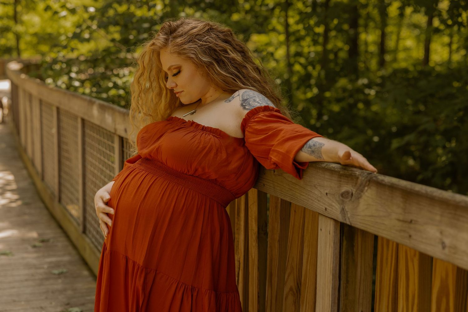 Maternity portrait in warm sunset light against rustic wooden railing.