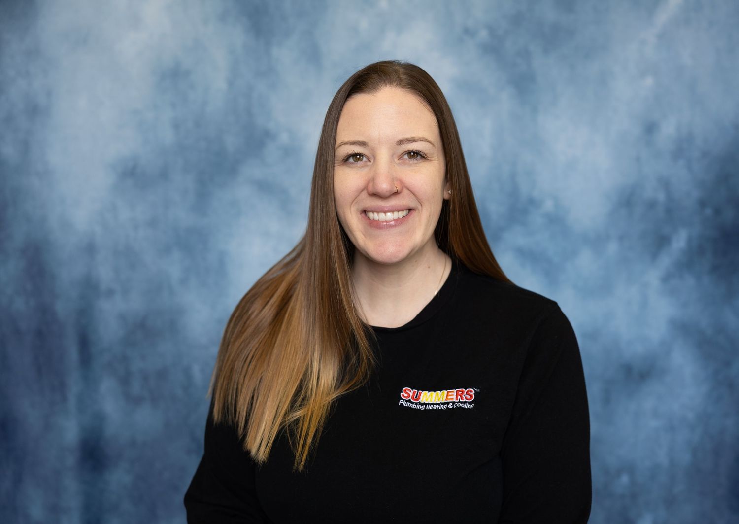 Smiling woman with long brown hair wearing a black Subway uniform shirt against a blue backdrop.