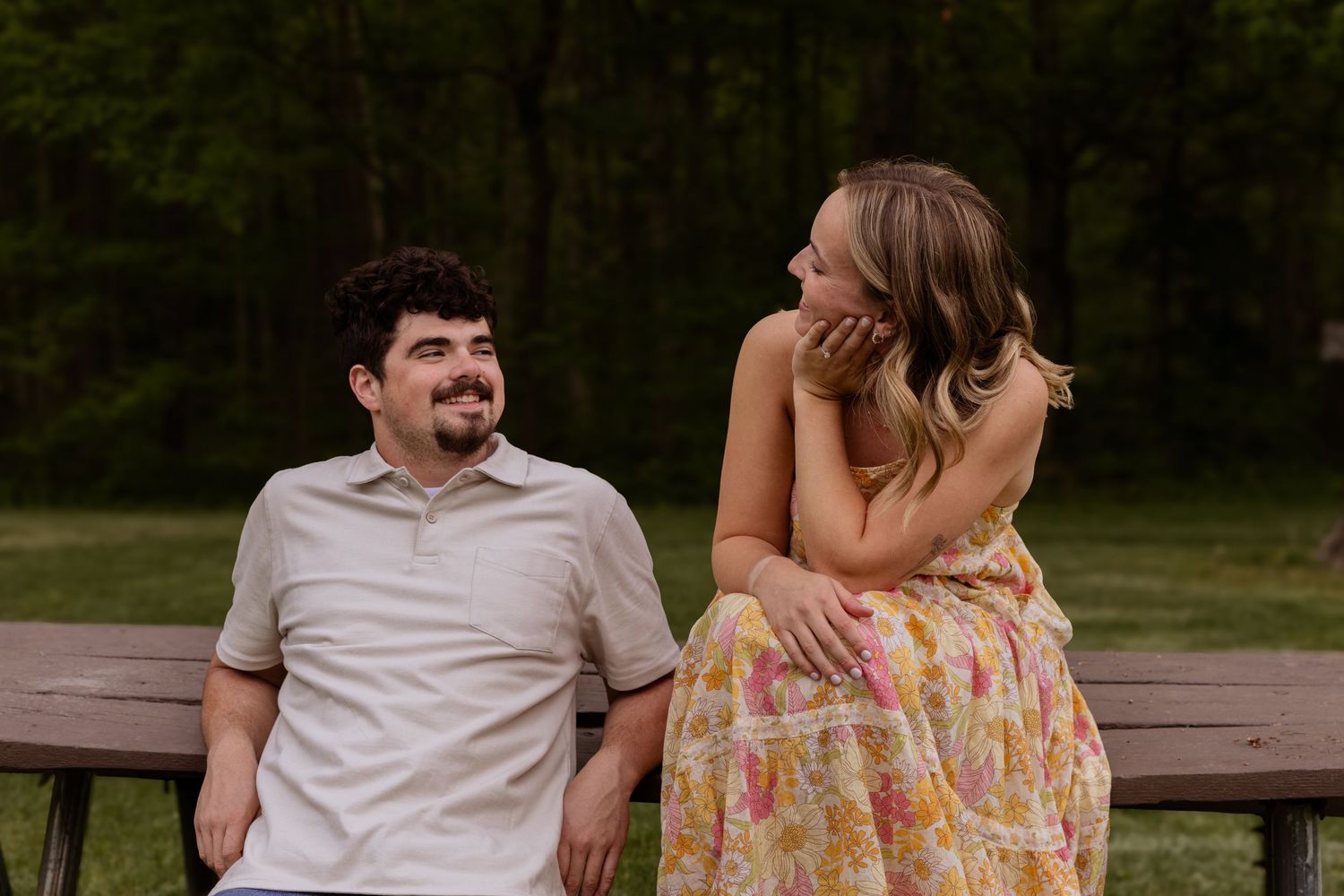 A couple in coordinated outfits embraces on a wooden bench in a park setting.